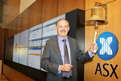 A man in a suit smiling and ringing a bell at the Australian Stock Exchange