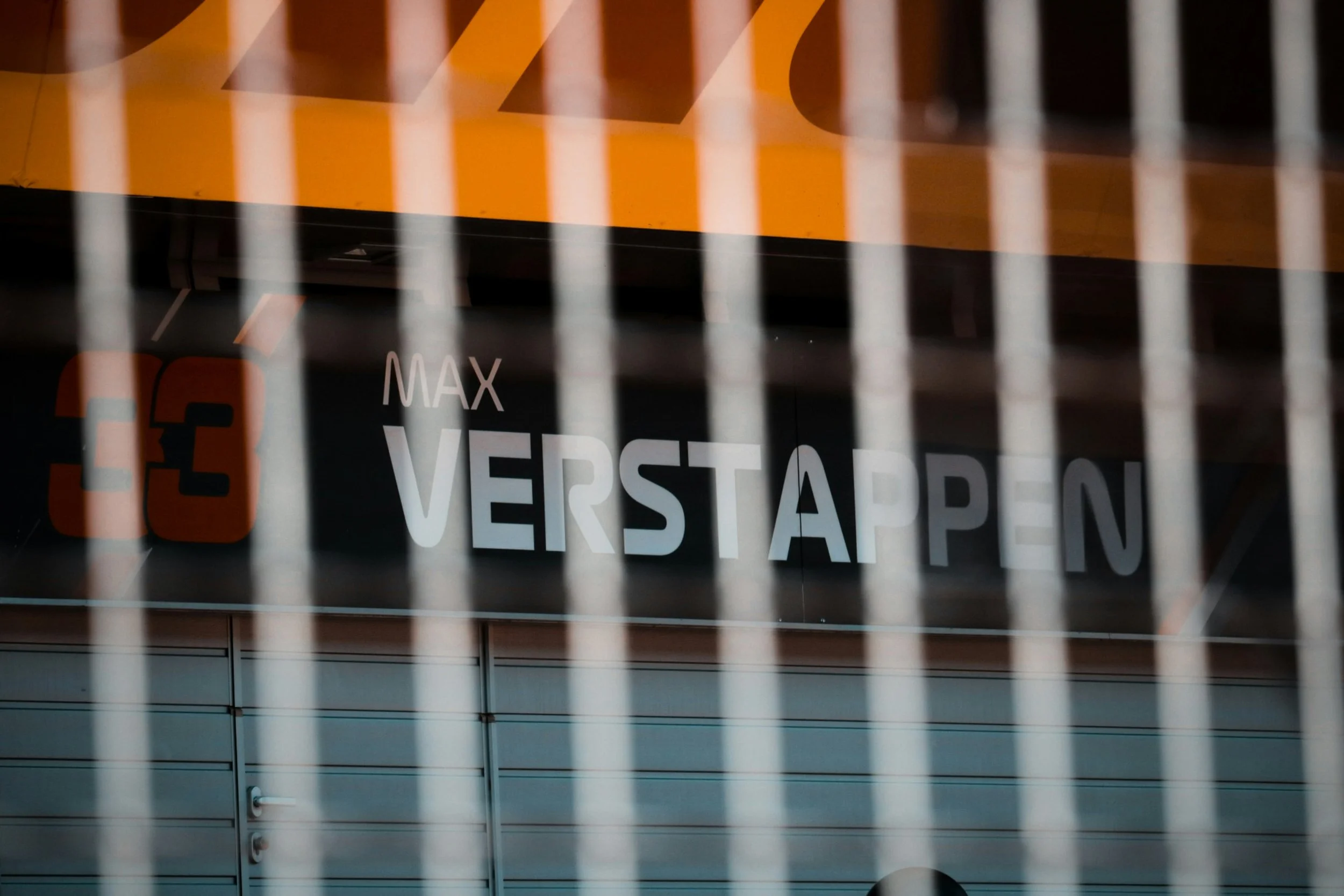 Max Verstappen Formula 1 garage signage viewed through pit lane fencing