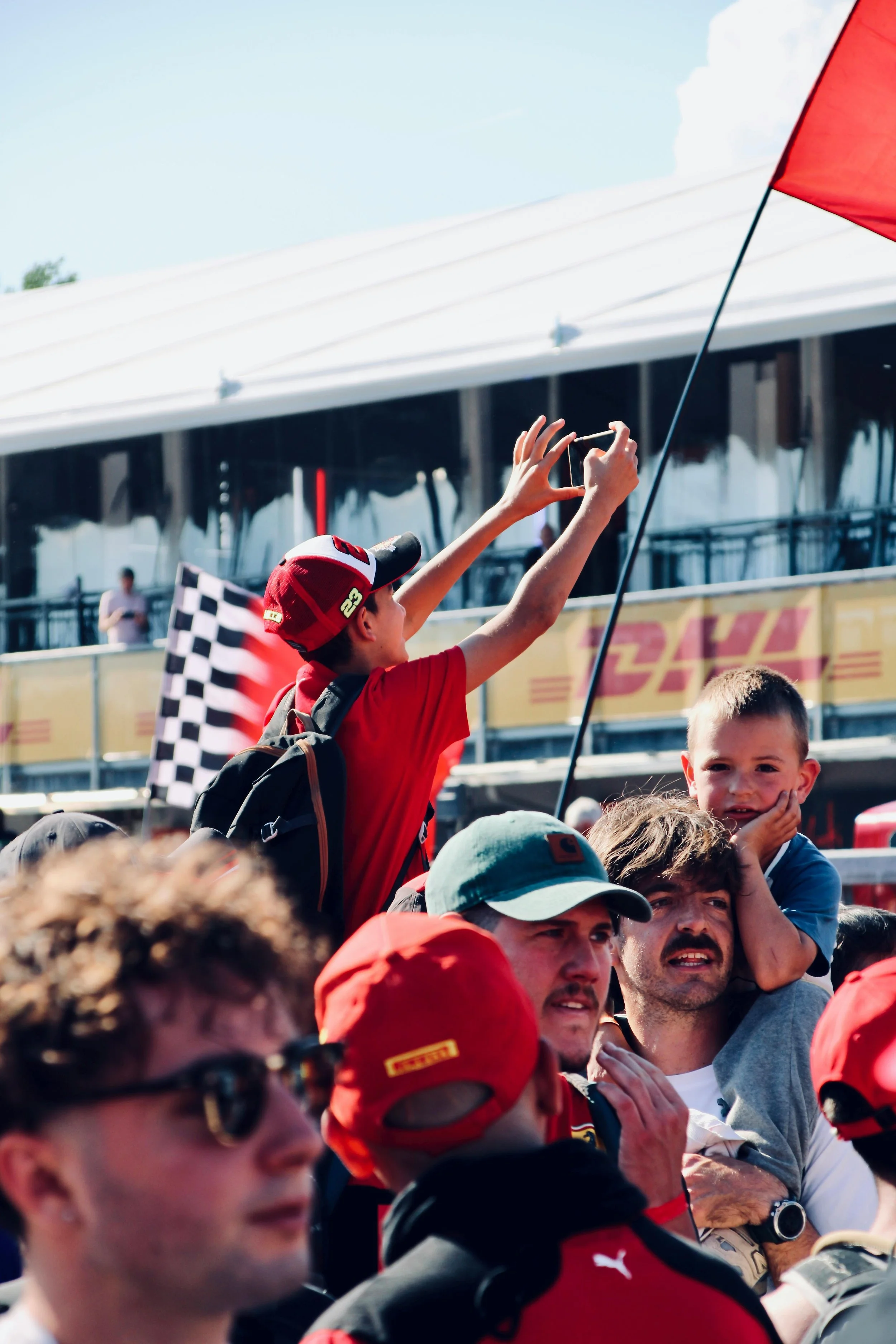 Formula 1 fans in a crowded grandstand taking photos and waving flags during a race weekend
