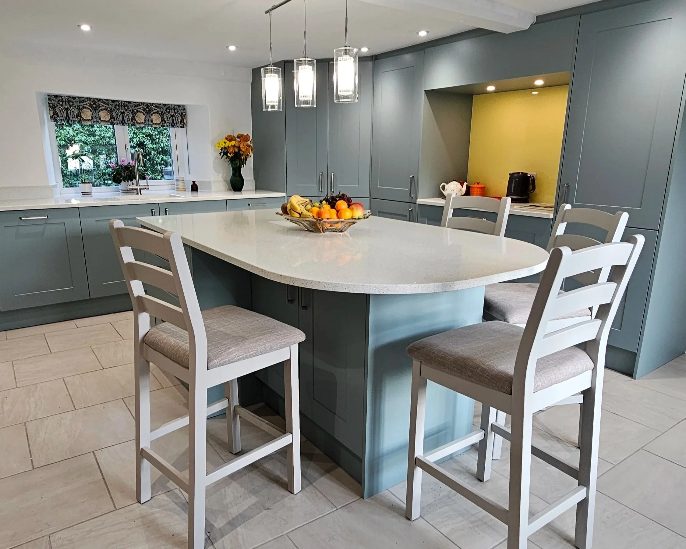 Modern kitchen with wood beams, gray lower cabinets, white upper cabinets, marble countertops, a window above the sink, and a wooden staircase leading to an upper level.