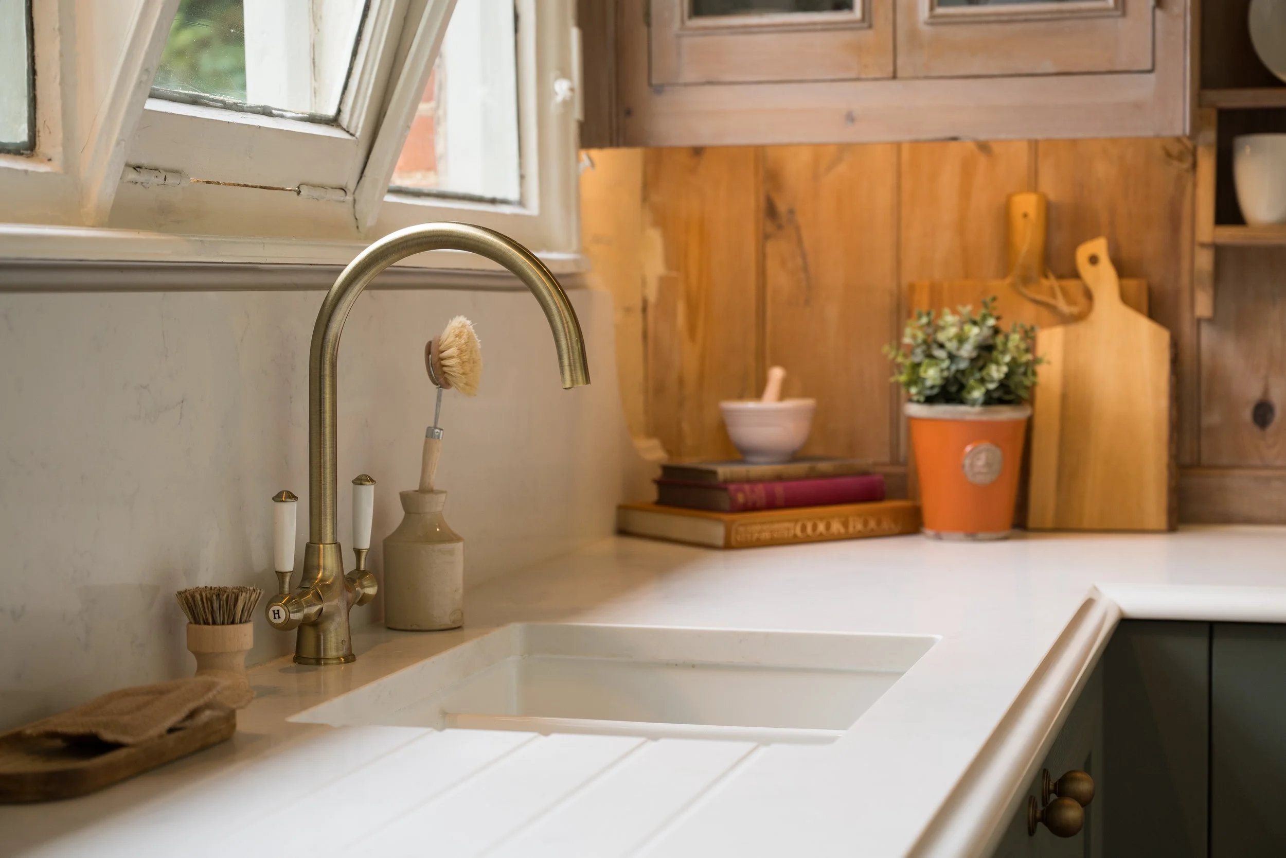 Rangemaster ceramic sink with Caple Shaftesbury brass tap and Carrara Branco quartz worktop beneath the original school window.
