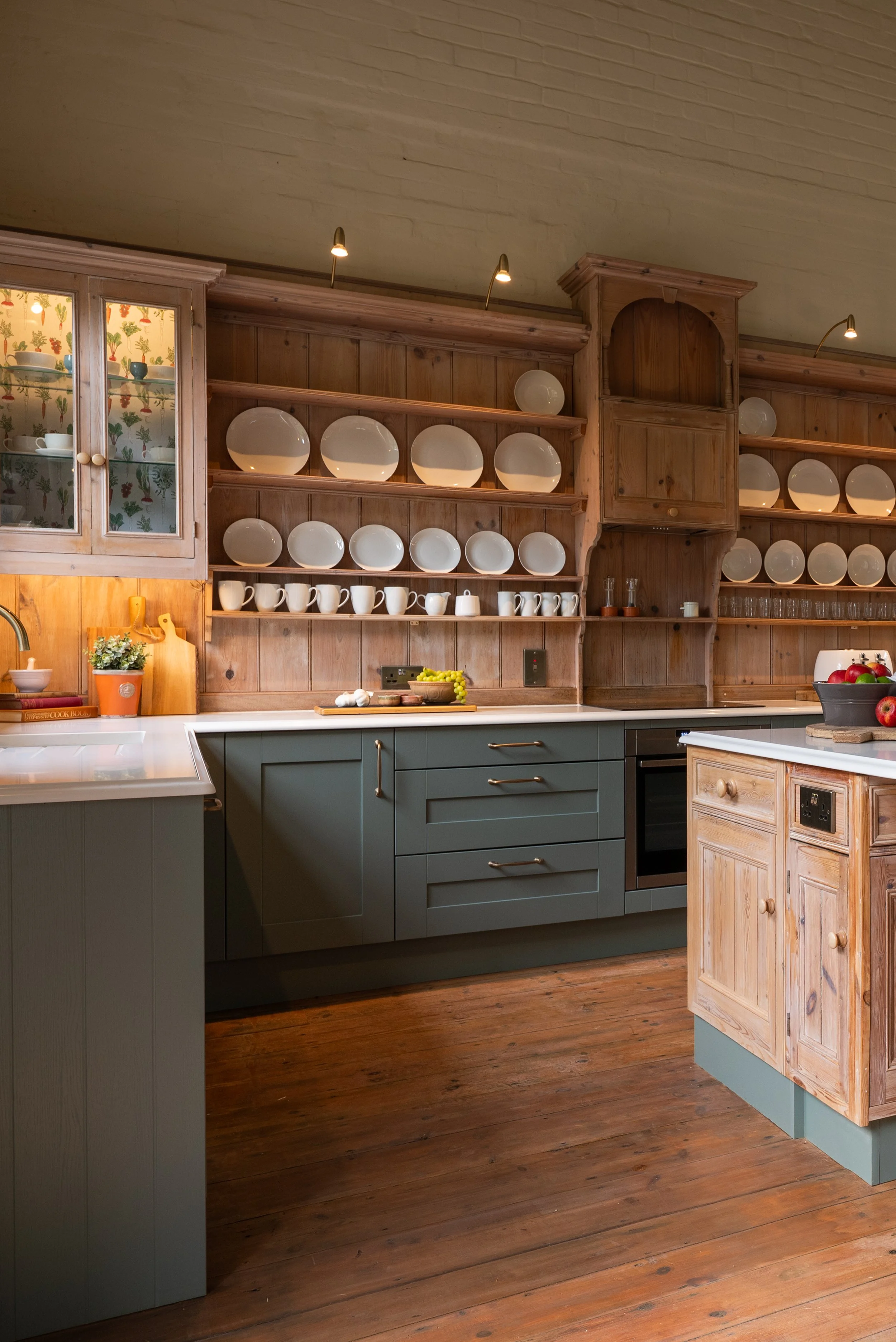 Kitchen in the former Great Snoring village school, with retained timber plate rack and central island made using reclaimed cabinetry.