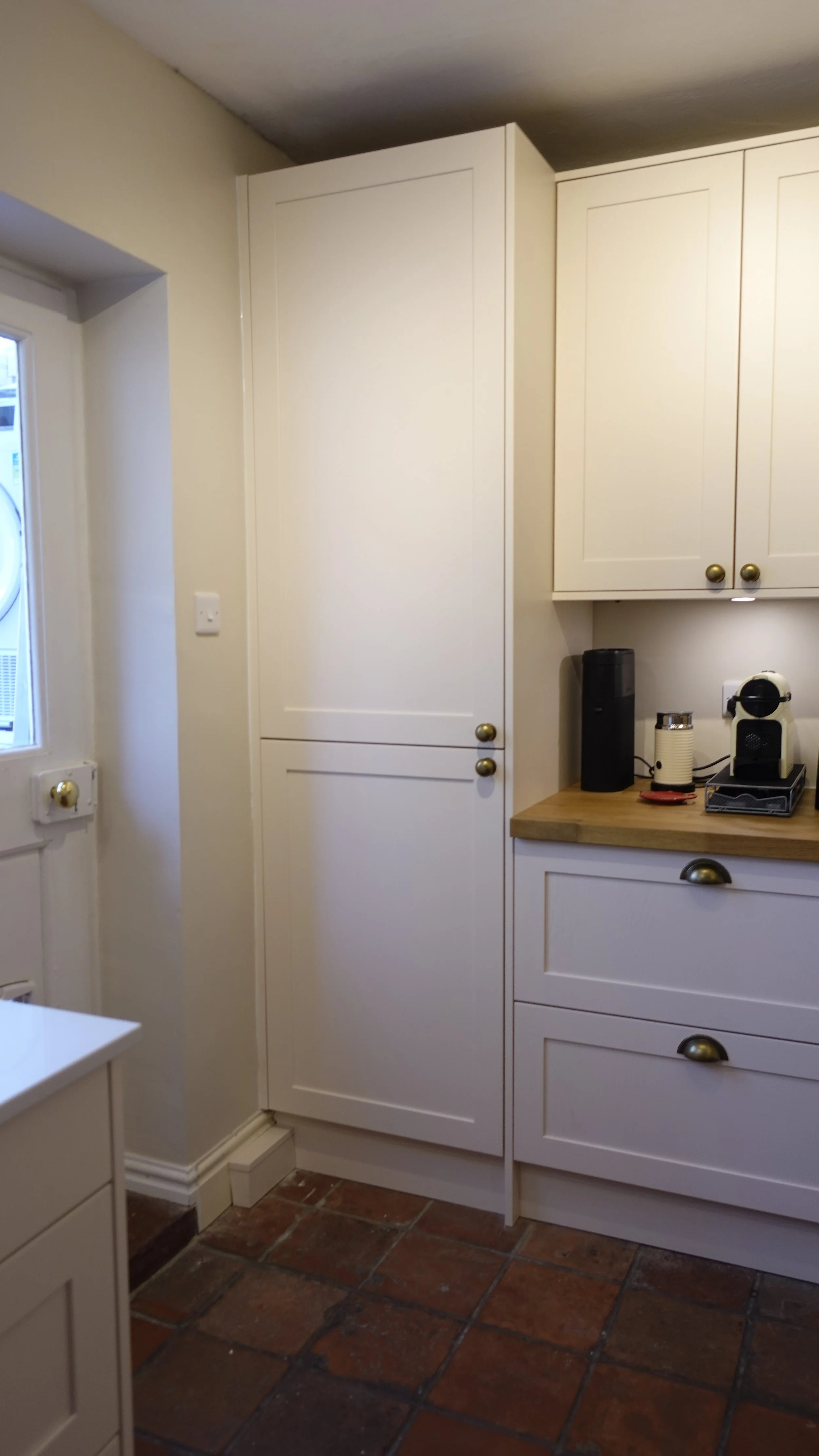 A kitchen corner with white cabinets, a window, and a countertop with a coffee machine and other small appliances.