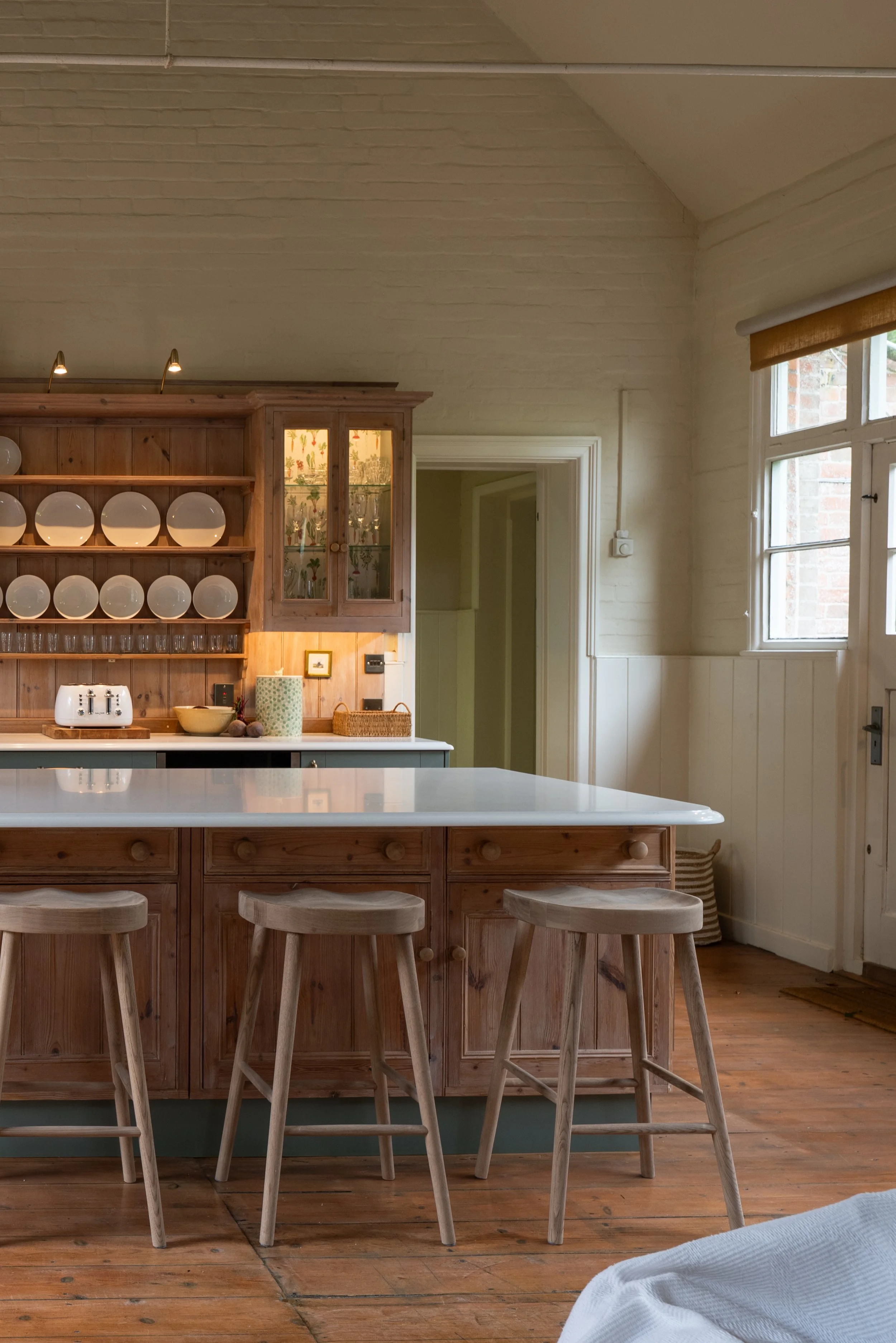 Reclaimed timber kitchen island with Carrara Branco quartz worktop, overlooking the retained plate rack and glazed cabinet in the Great Snoring School House.
