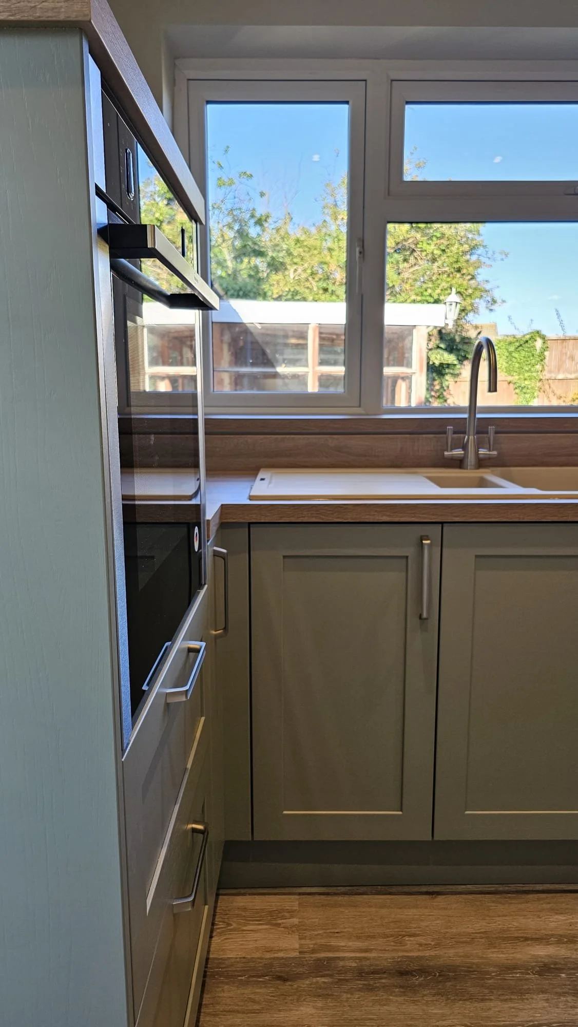 Kitchen with grey cabinets, a wooden countertop, a window above the sink, and a built-in oven.