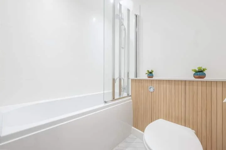 A clean, modern bathroom with a white bathtub, a wooden panel wall, and two small potted plants on a ledge.