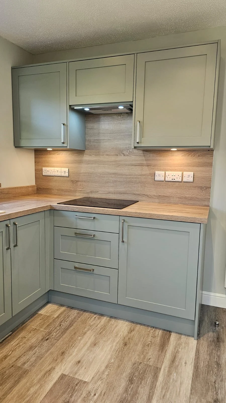 Kitchen with light green cabinets, wooden countertop and backsplash, black cooktop, and multiple electrical outlets.