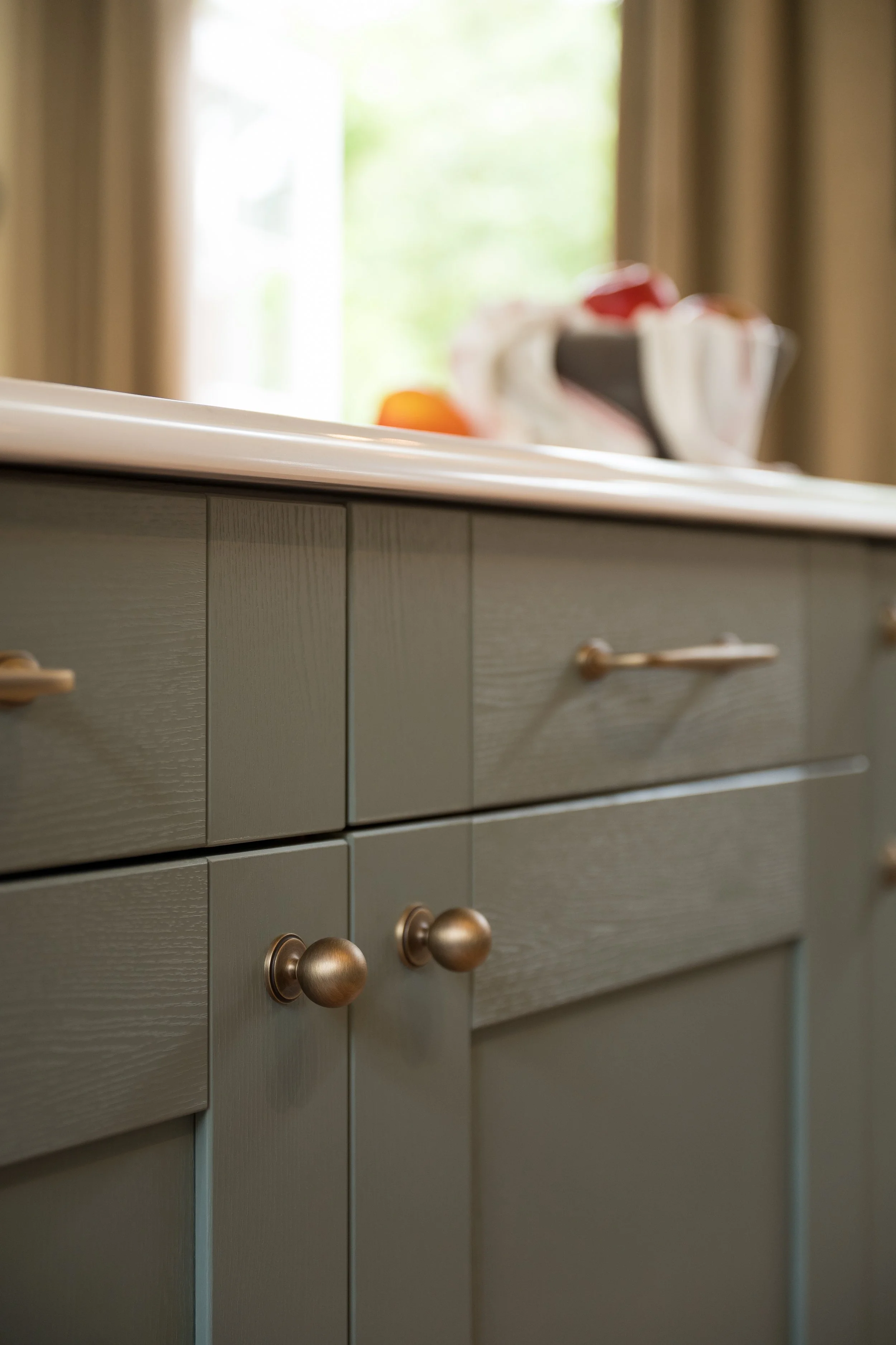 Carrara Branco quartz worktop with bespoke ogee edge above Reed Green Shaker cabinetry and brass handles.