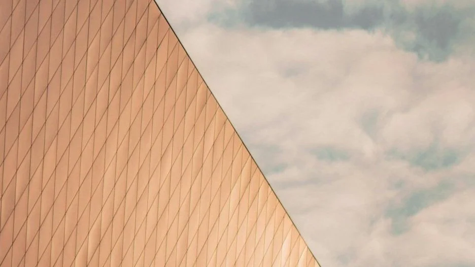 A close-up photo of a building with a geometric, diamond-patterned exterior, against a cloudy sky. Bespoke stretch ceiling lighting custom designs.