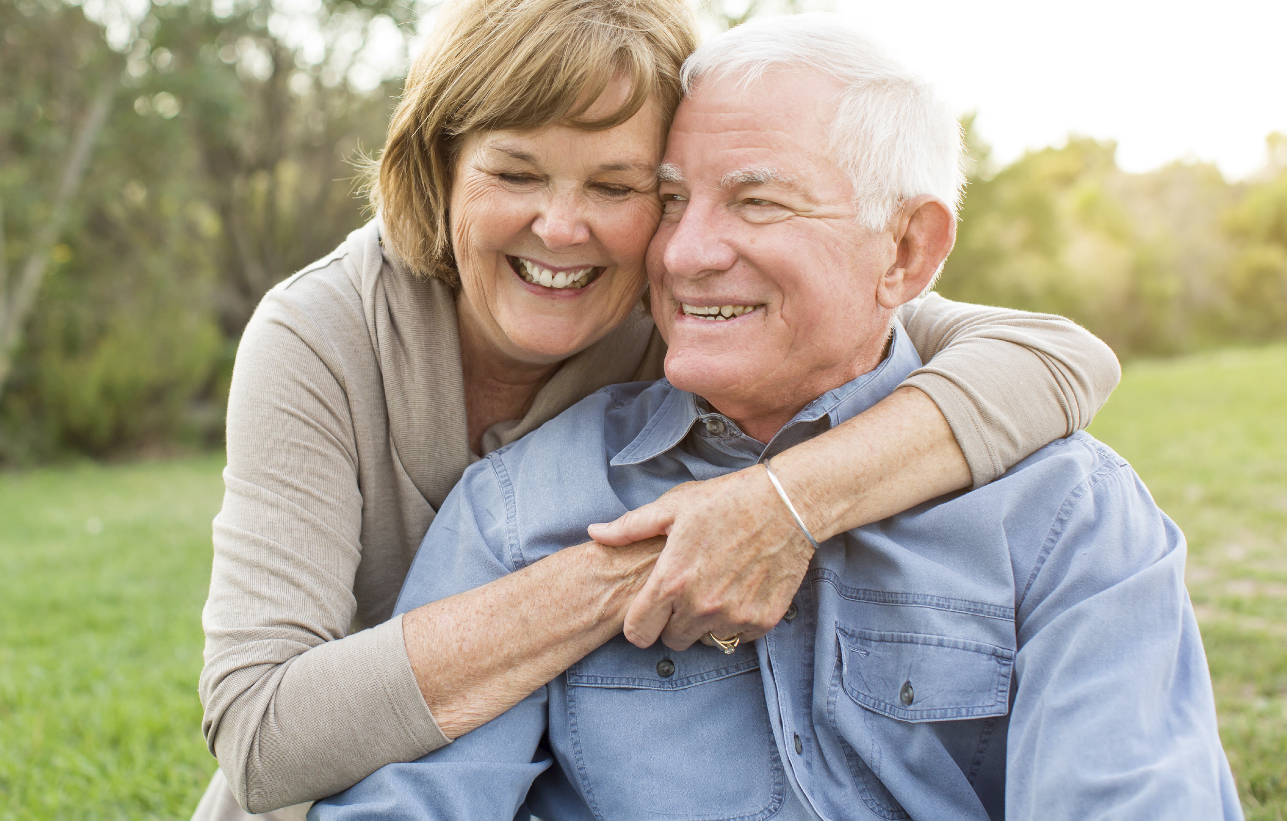 A smiling older man being hugged by a family member