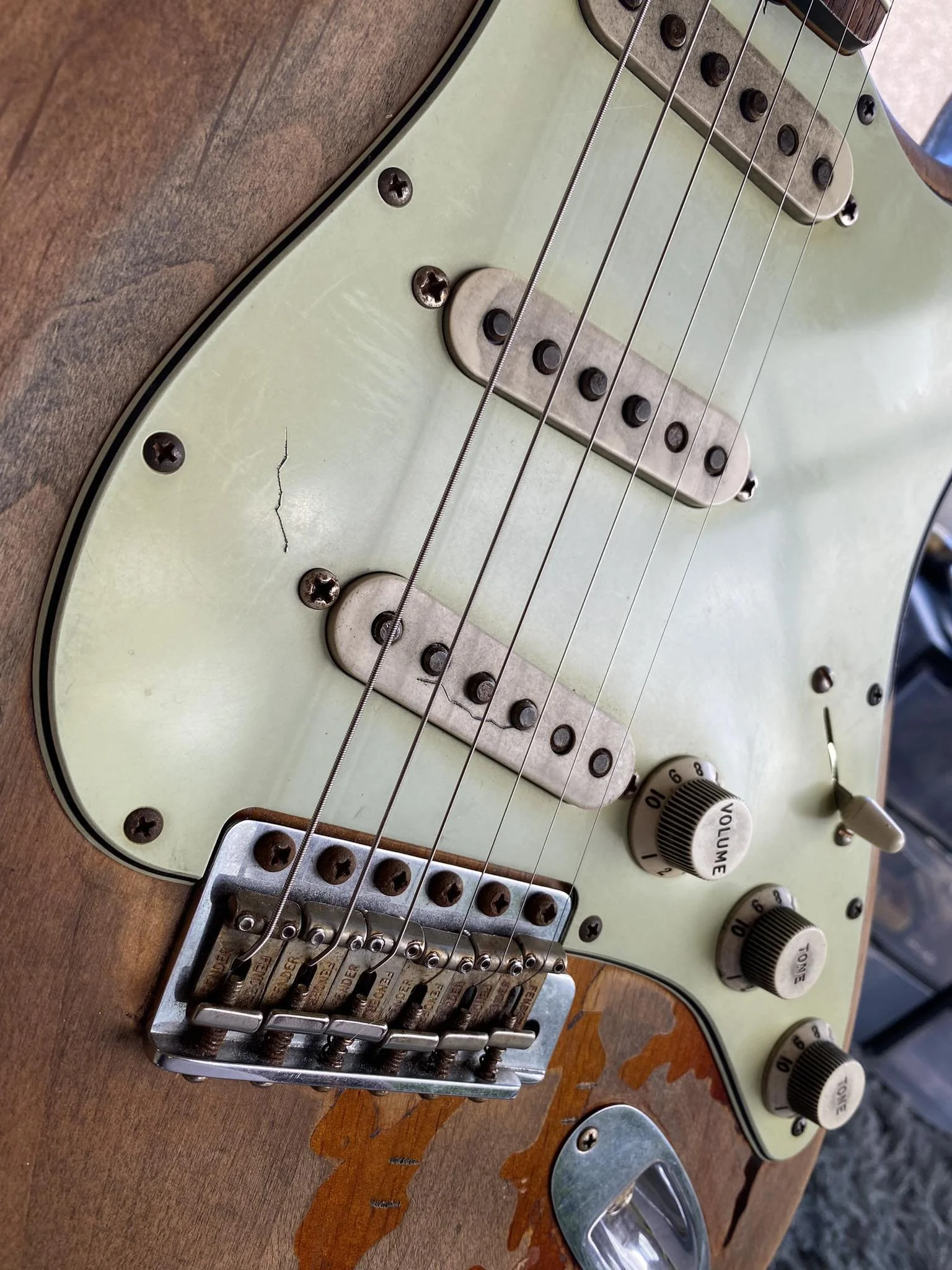 Close-up of an electric guitar with visible scratches, rust, and wear on the body, pickups, and bridge.