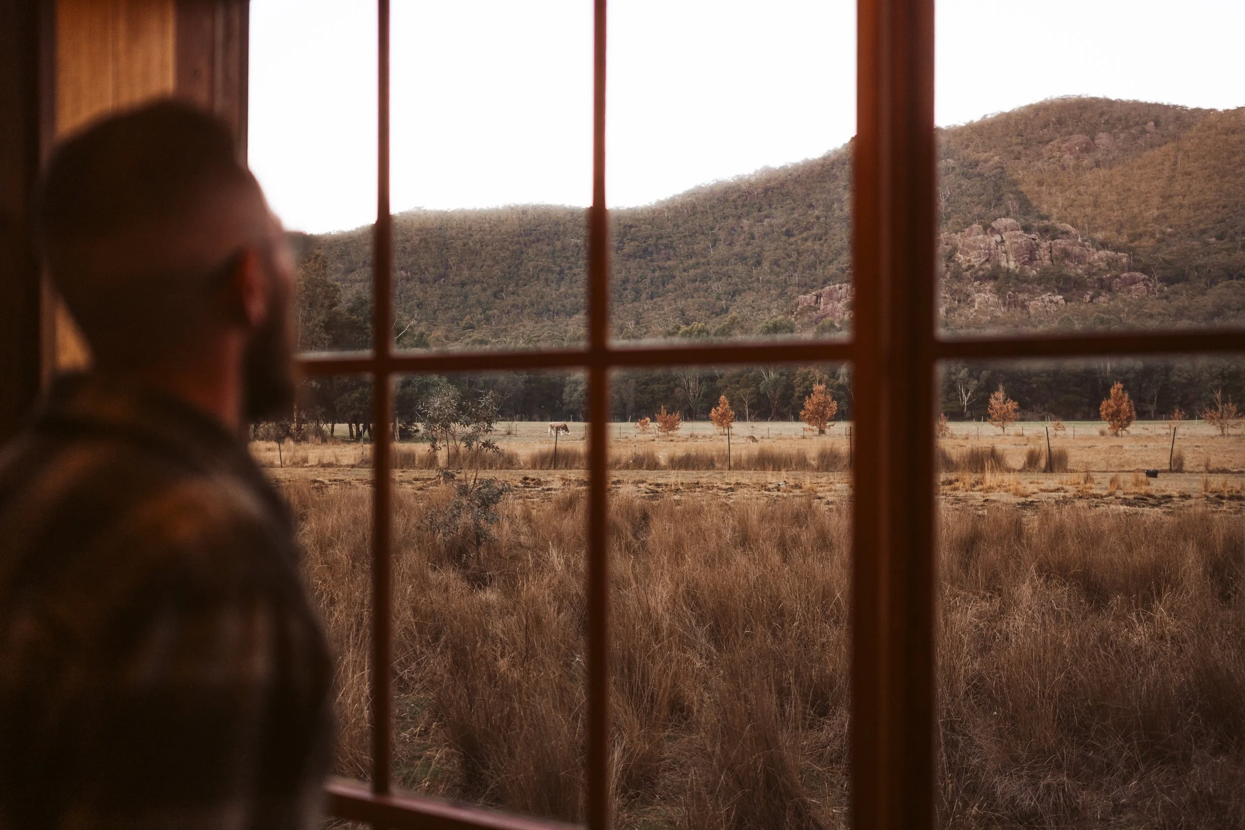 Looking through the window of an off-grid tiny hut towards the mountains of the Grampians near Halls Gap, Victoria.
