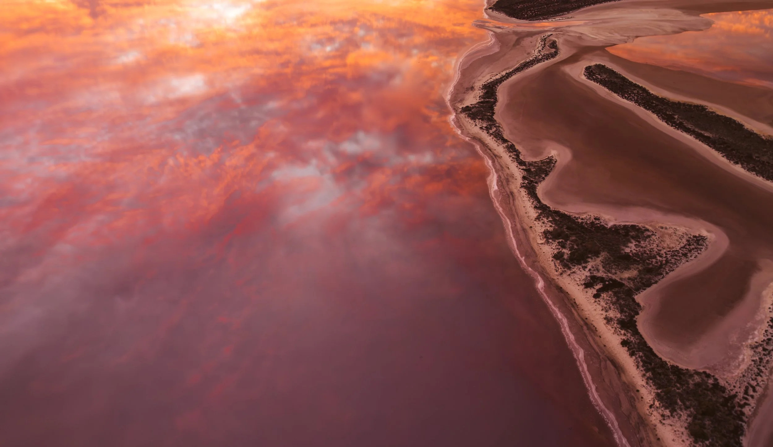 Aerial view of Lake Tyrrell at sunrise, with pink water reflecting orange clouds across the salt lake in Victoria.