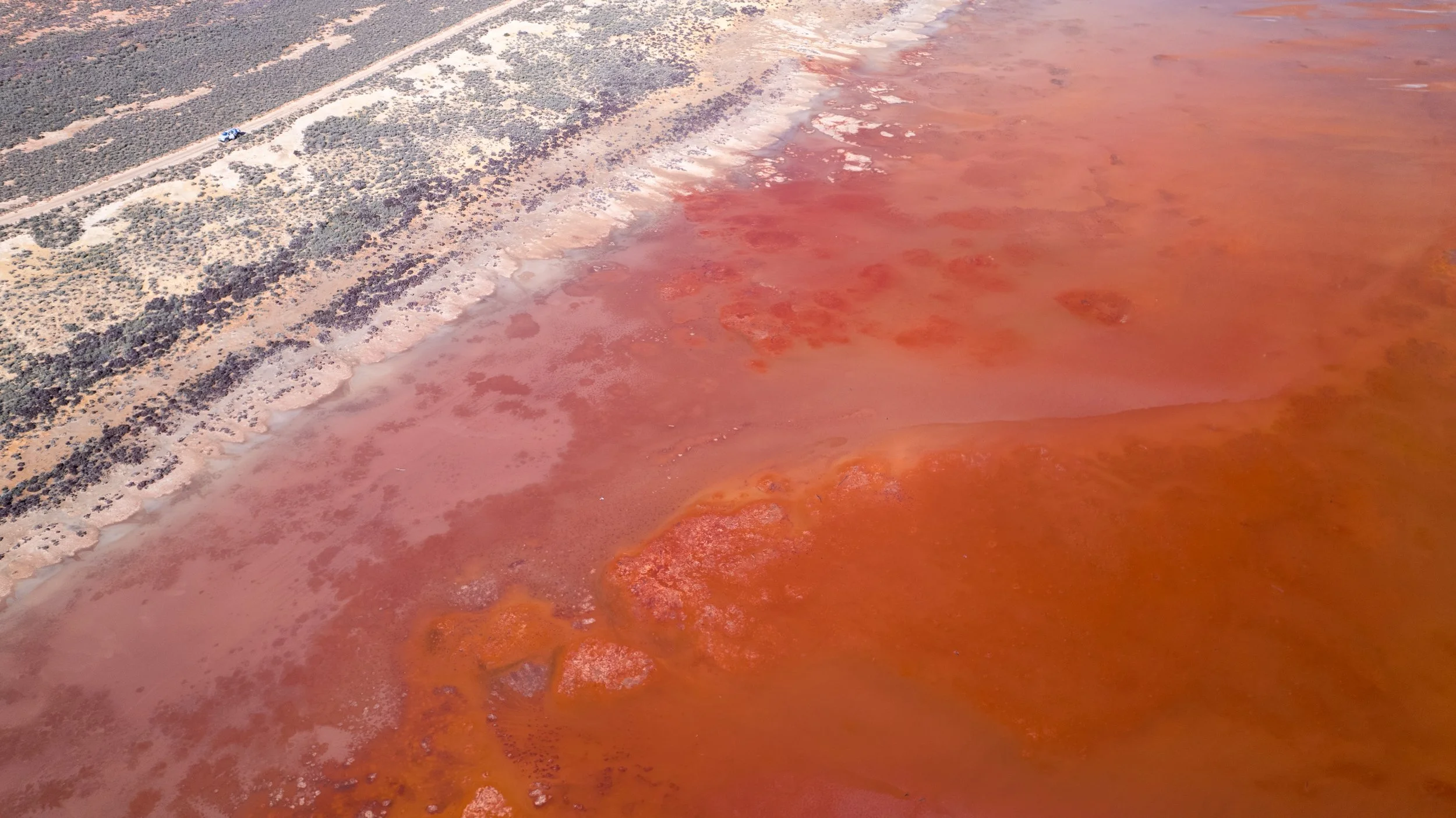 Aerial view of the vivid pink and orange salt water of Lake Tyrrell, surrounded by the dry Mallee landscape in Victoria.