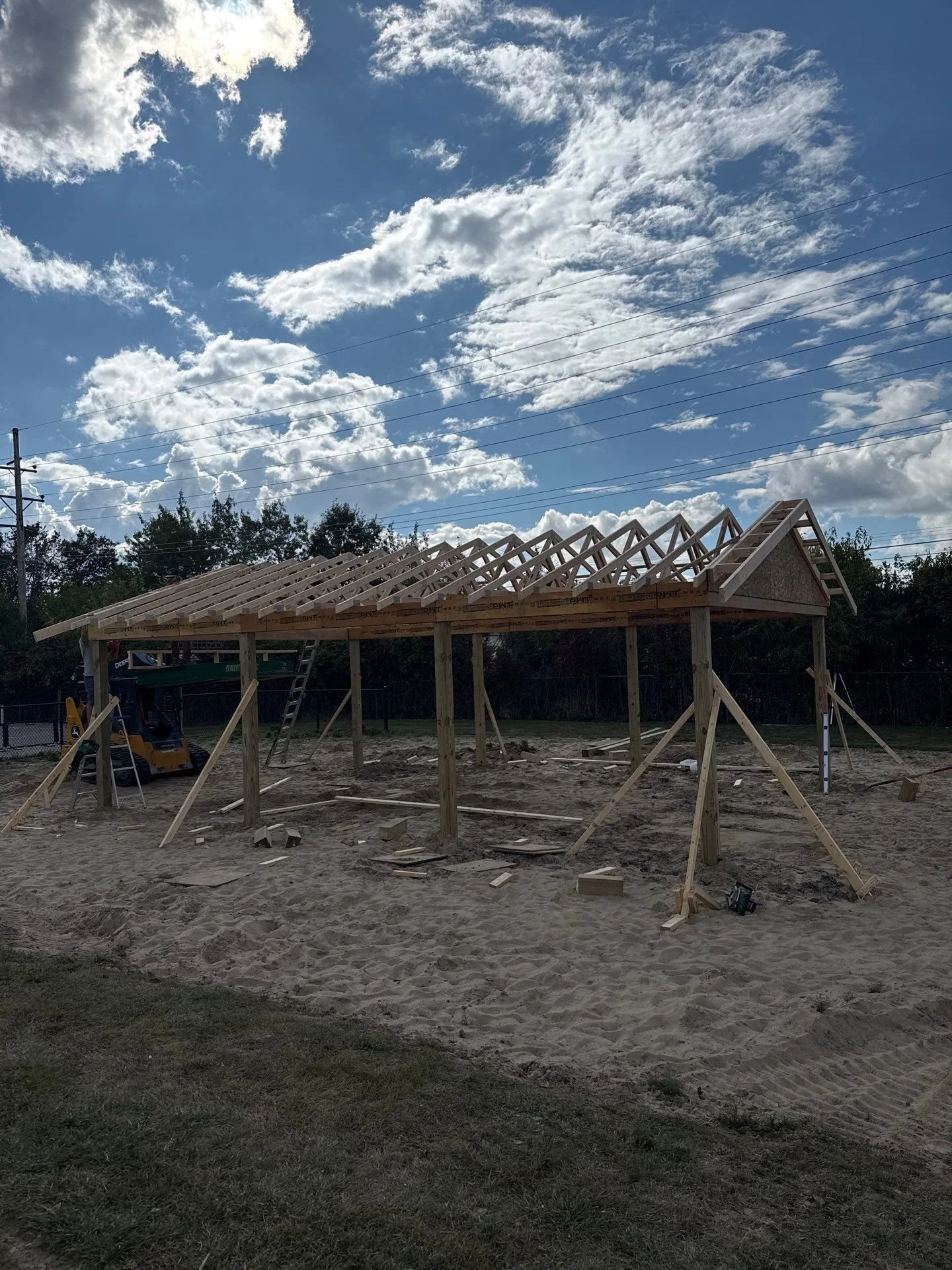 Under construction wooden structure frame in a sandy area with a partly cloudy sky