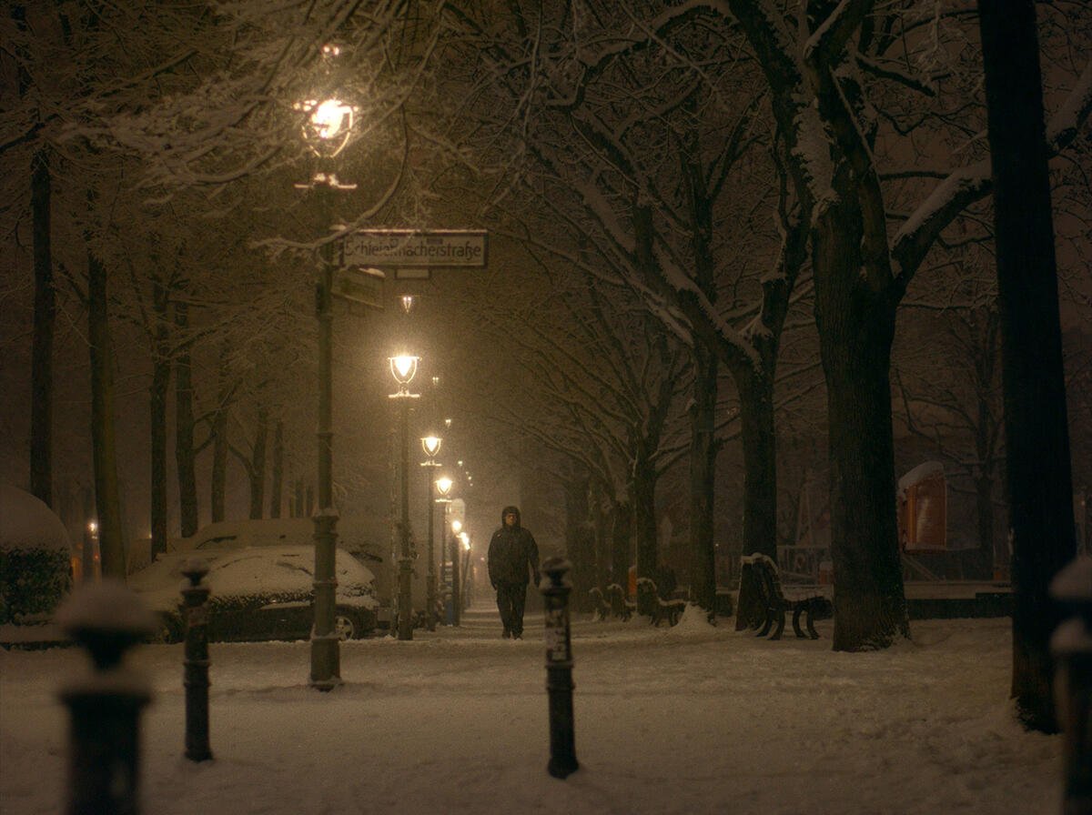 Still from A Letter to Home (2026), cinematography by Dorothea Pilz: a lone figure walking beneath street lamps in a winter park at night
