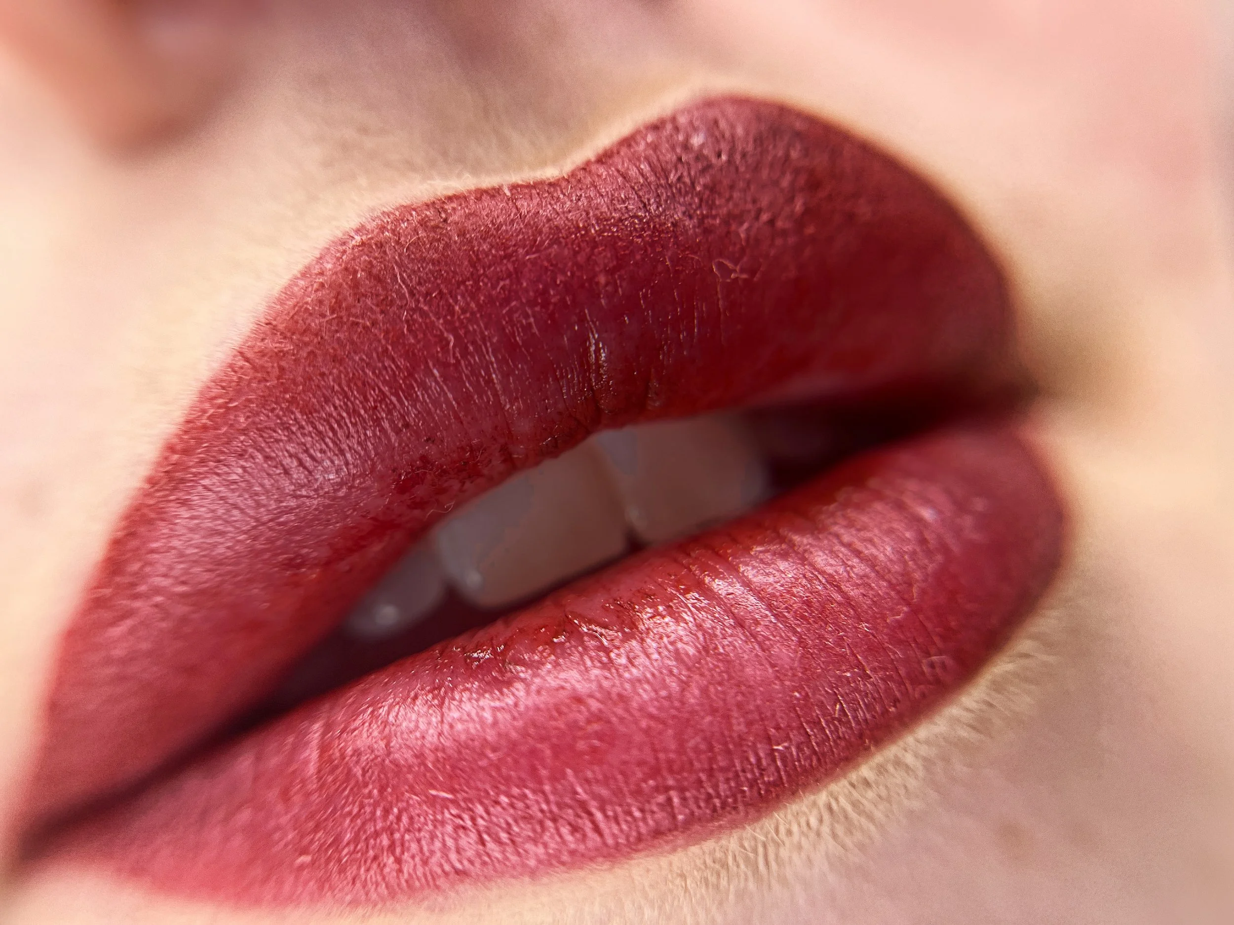 Close-up of lips wearing deep red lipstick, slightly parted showing teeth.