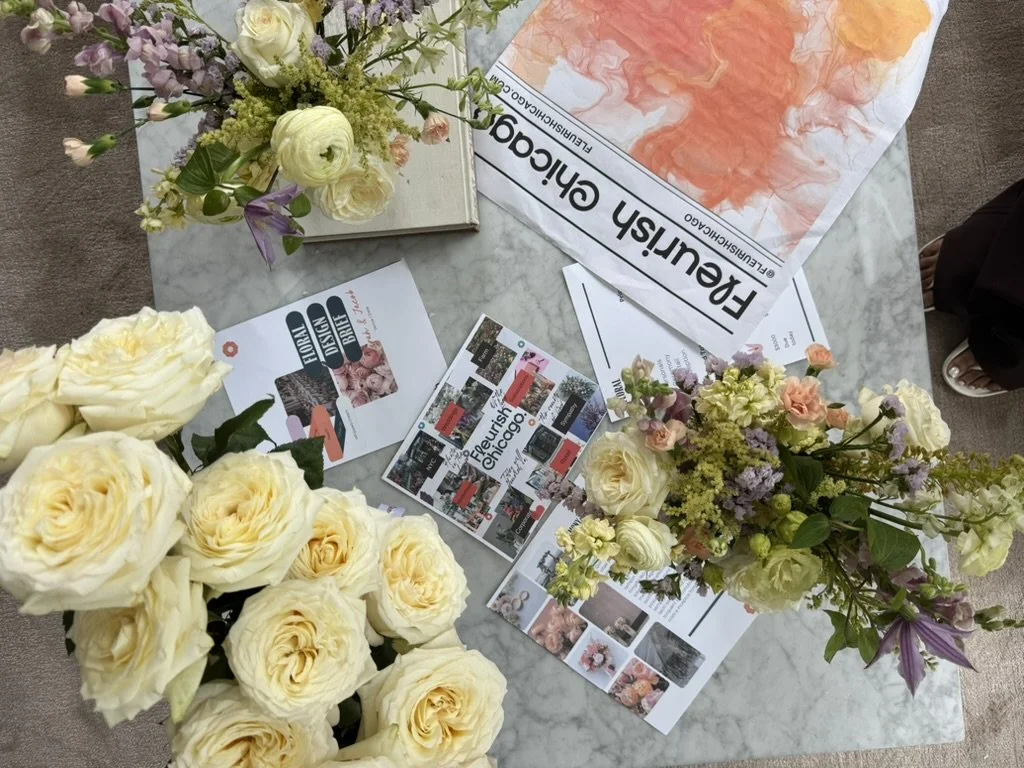 A marble table with floral arrangements of cream, purple, and peach flowers, and various informational flyers and posters about Chicago and floral design.