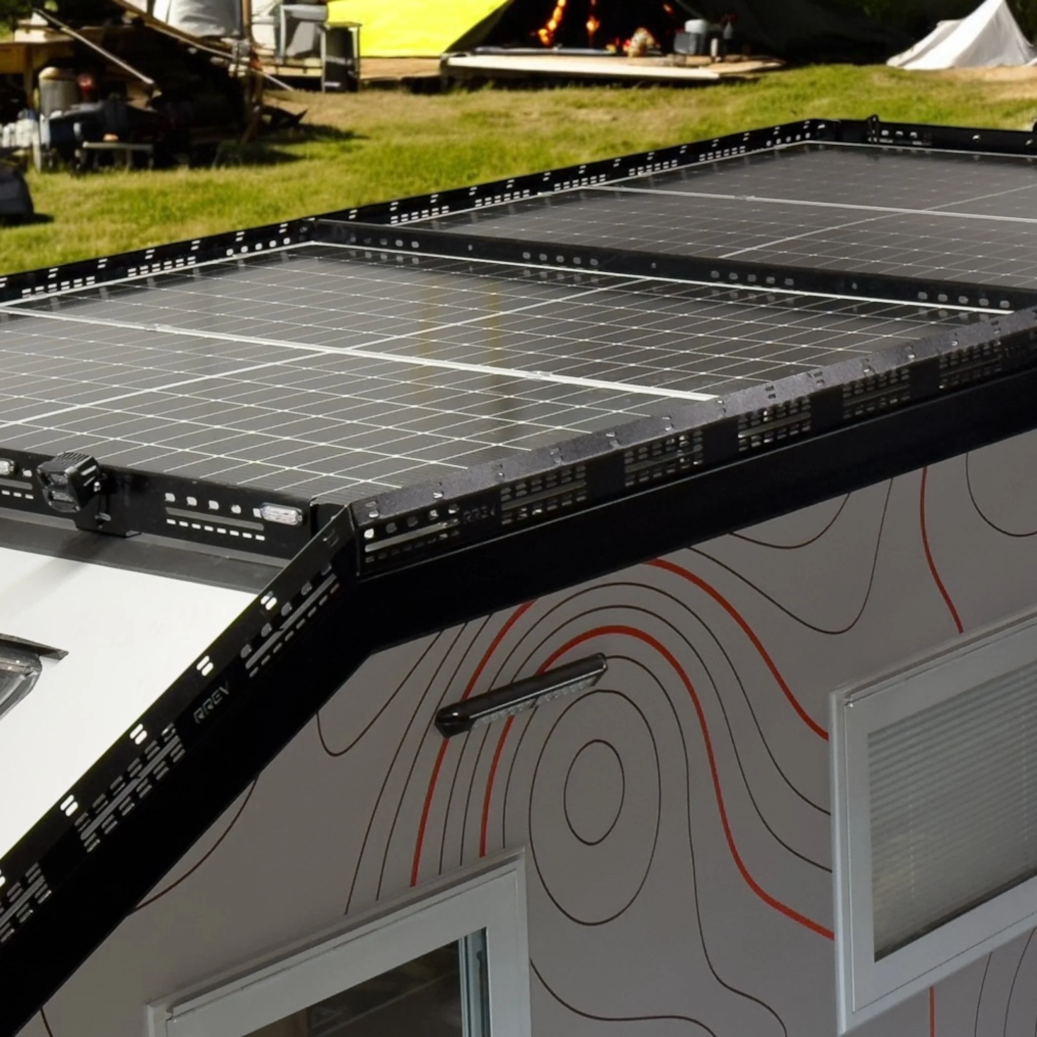 A travel trailer with solar panels on the roof parked on a sandy area surrounded by pine trees.