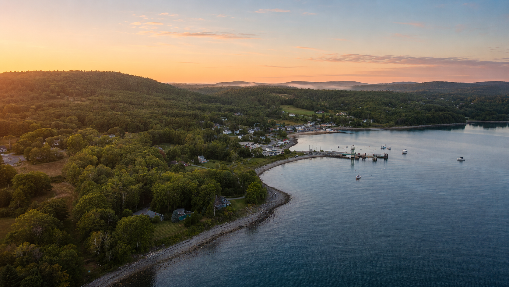 Aerial view of Lincolnville Beach, Maine at sunset with boats in the water and lush green hills in the background.