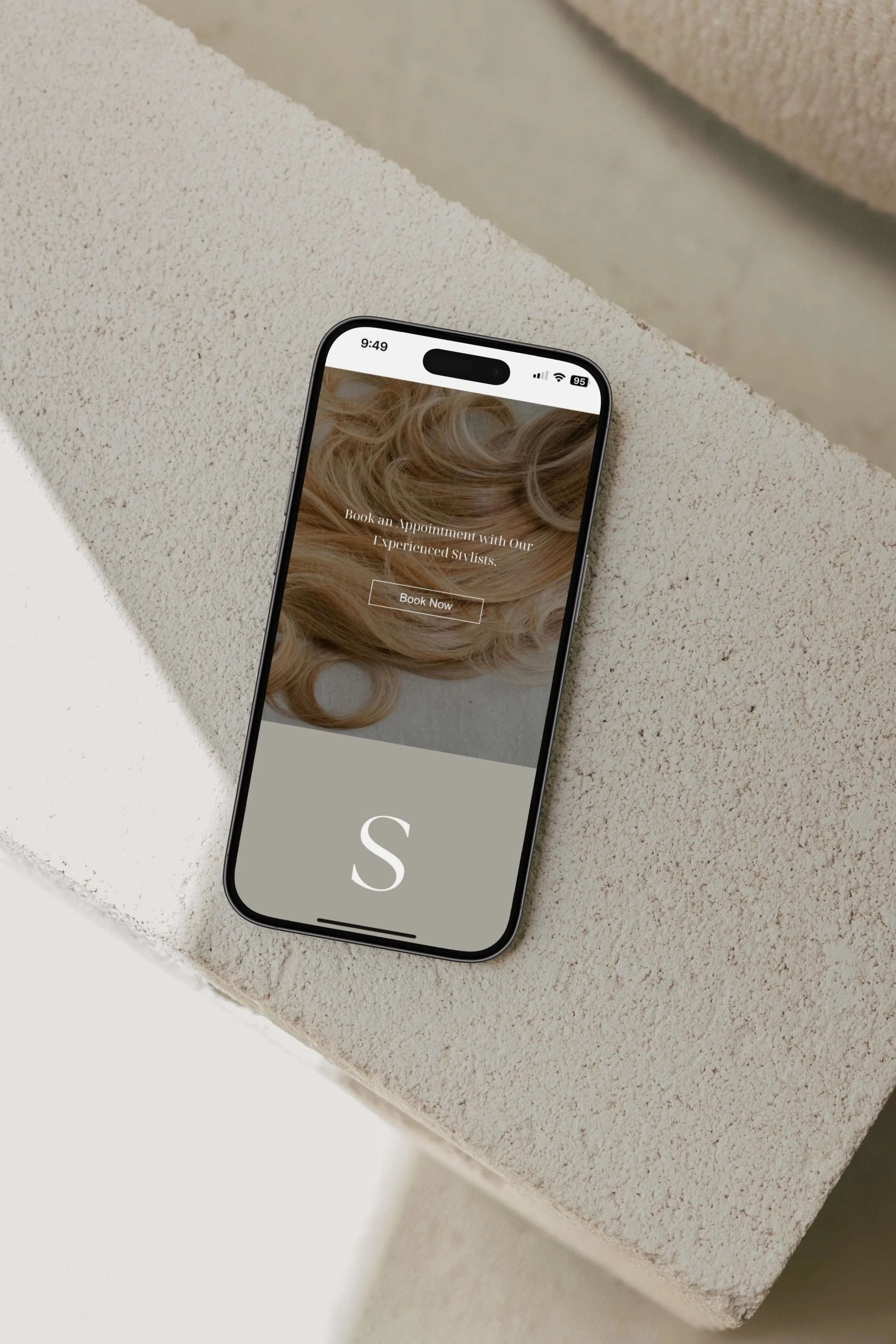 Smartphone displaying a website for booking hair appointments, with an image of blonde curls and a large letter 'S' at the bottom.