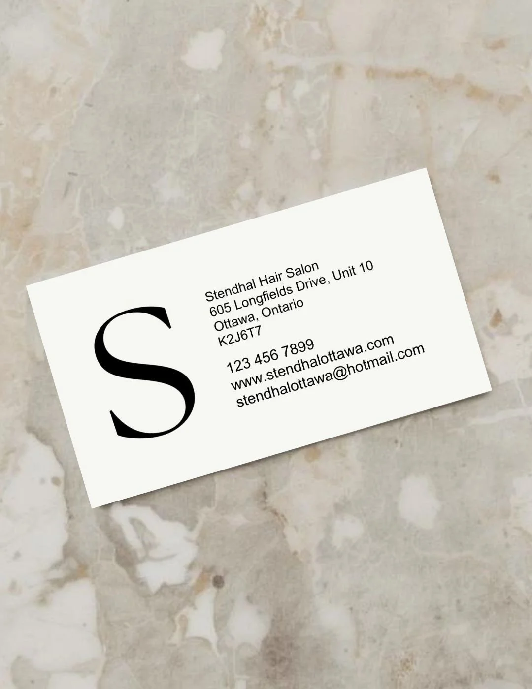 Business card for Stendhal Hair Salon with large letter S and contact information on a light-colored tile surface.