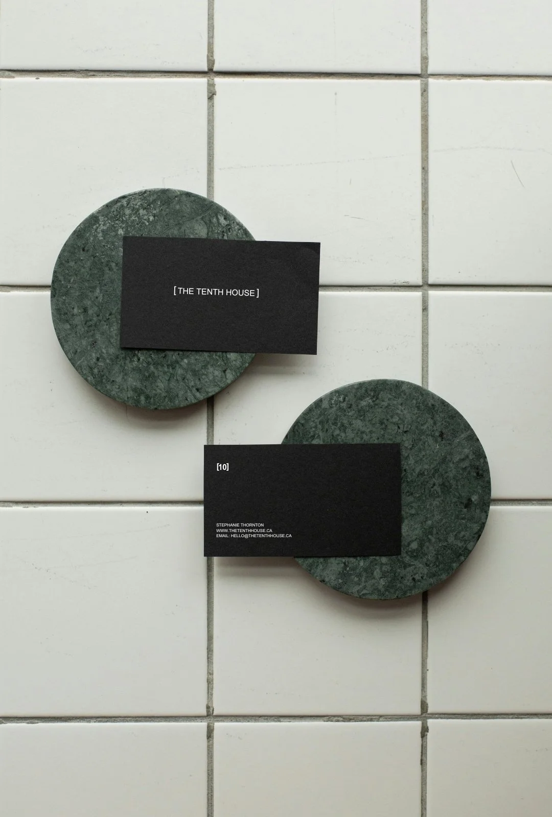 Black business cards with white text on green marble coasters placed on white tiled surface.