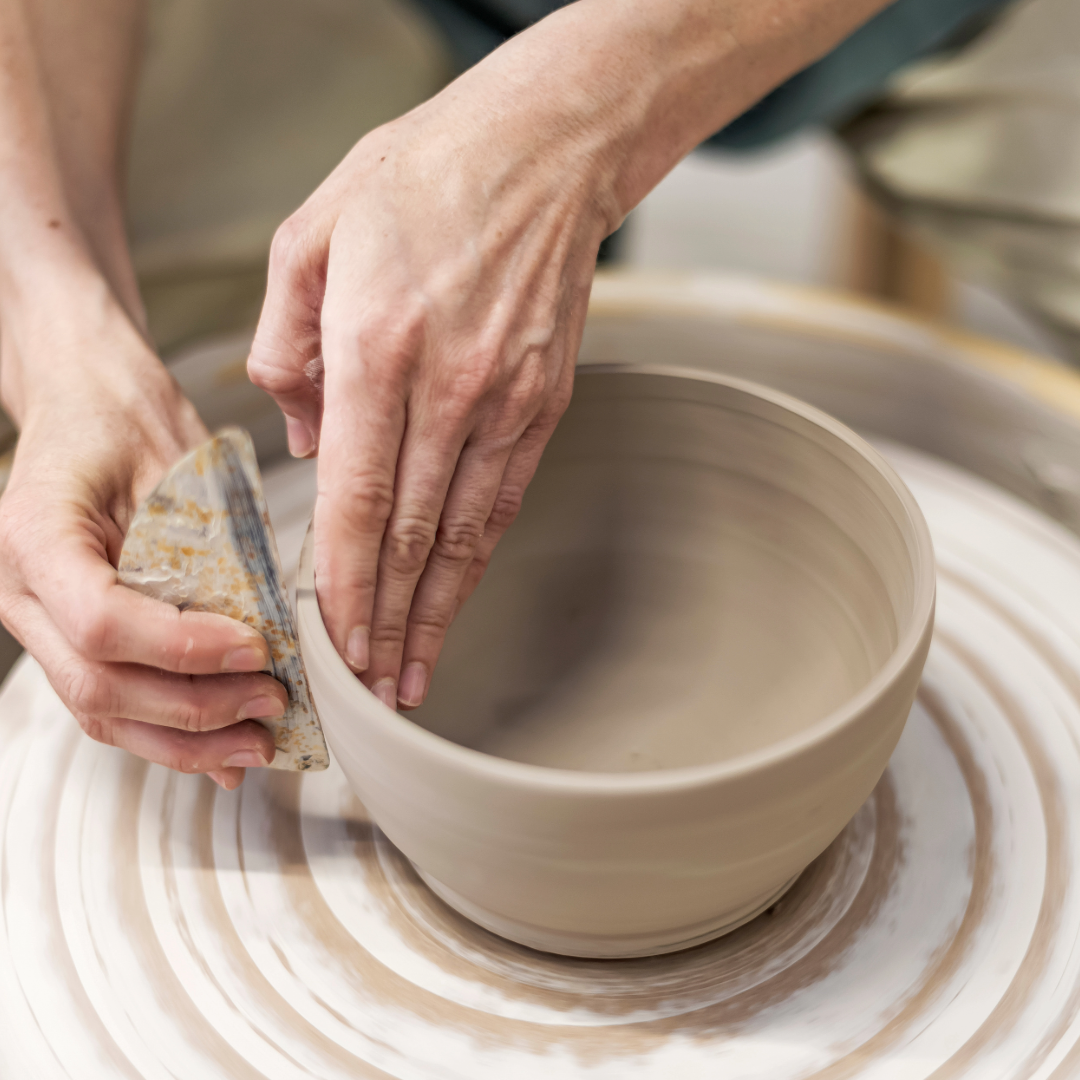 Hands shaping a ceramic bowl on a pottery wheel while smoothing the surface with a sponge.