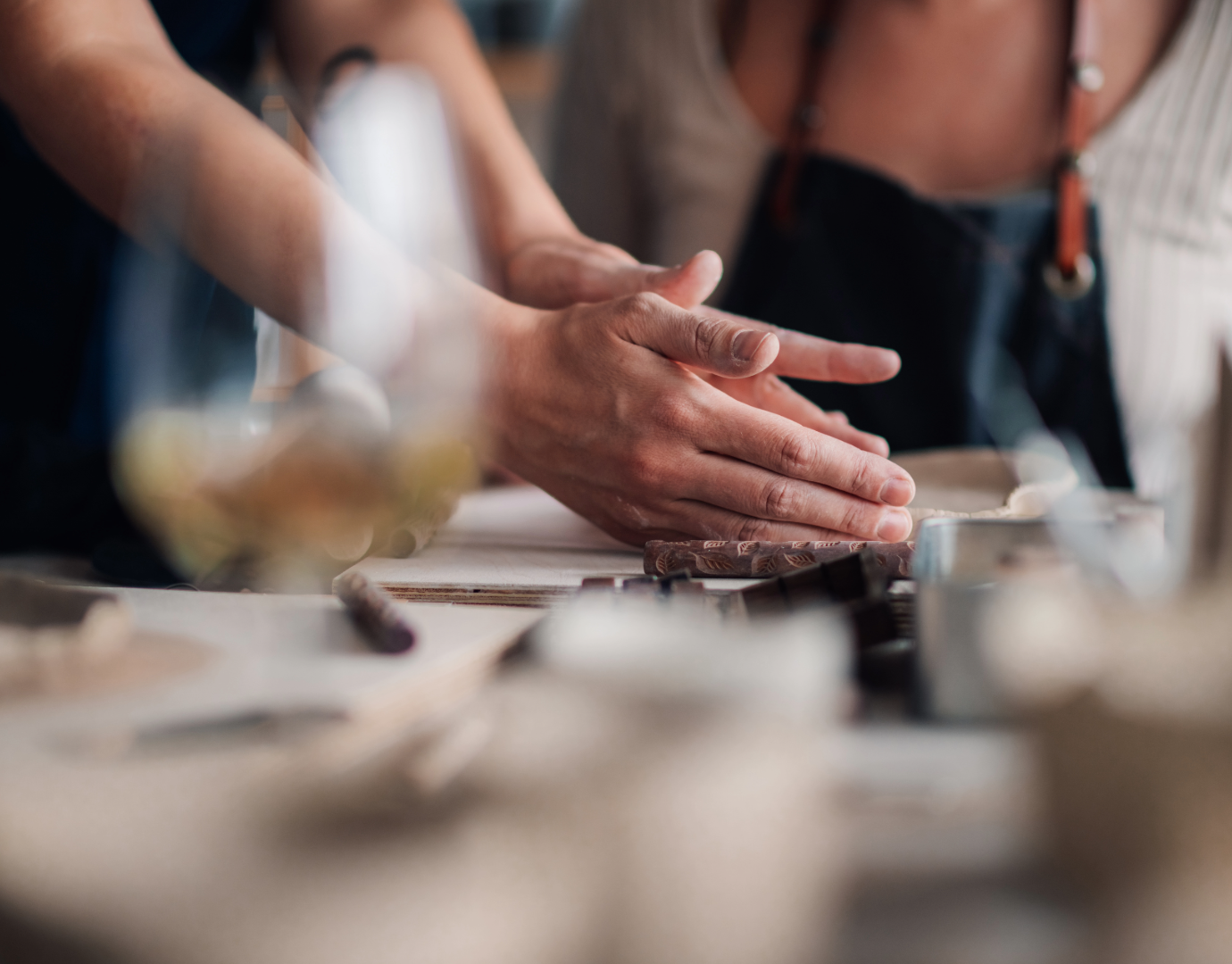 Hands kneading dough on a cutting board in a kitchen, with person wearing an apron visible in background.