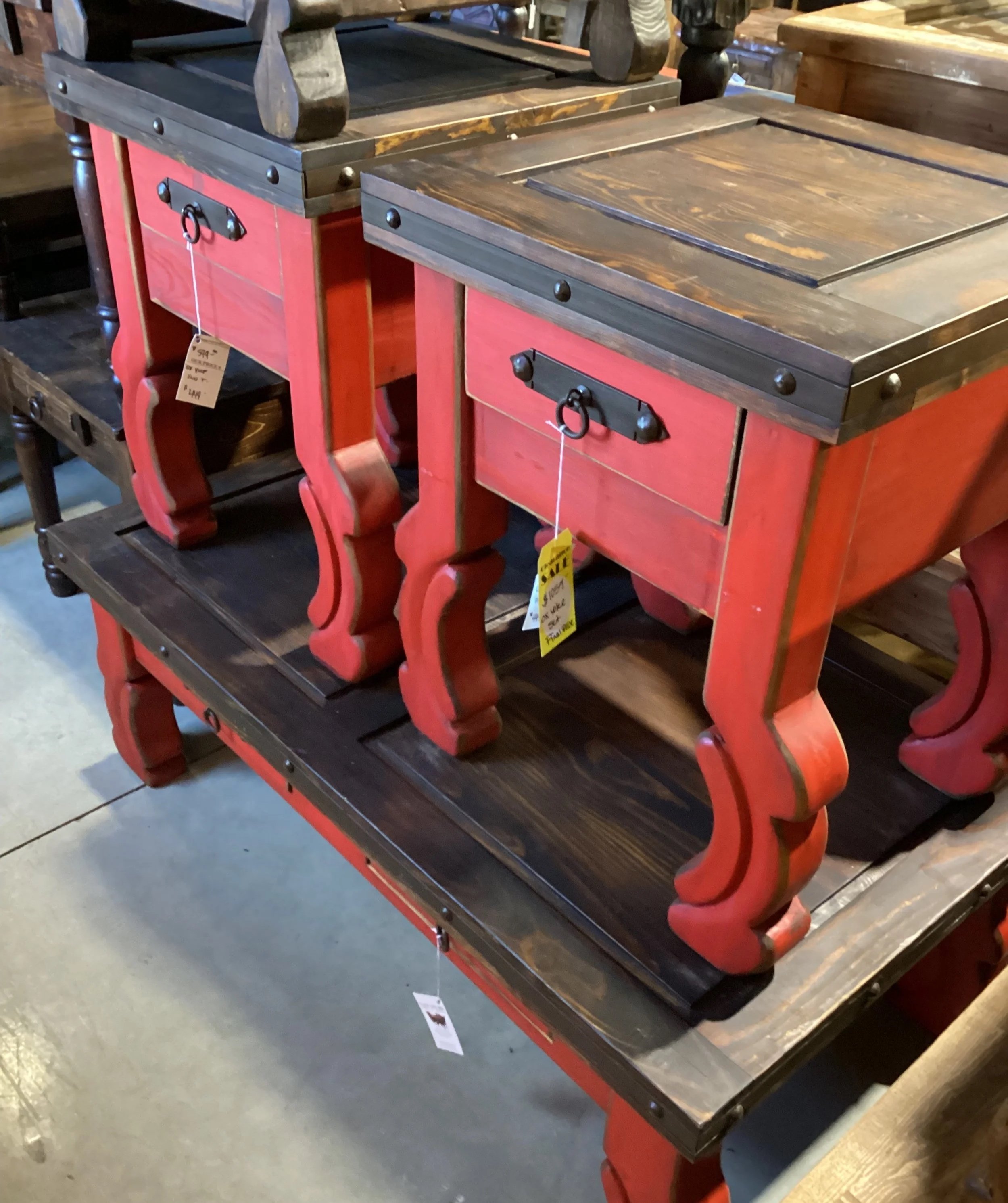 Set of two small wooden tables with red painted legs and dark brown tops, displayed in a furniture store.
