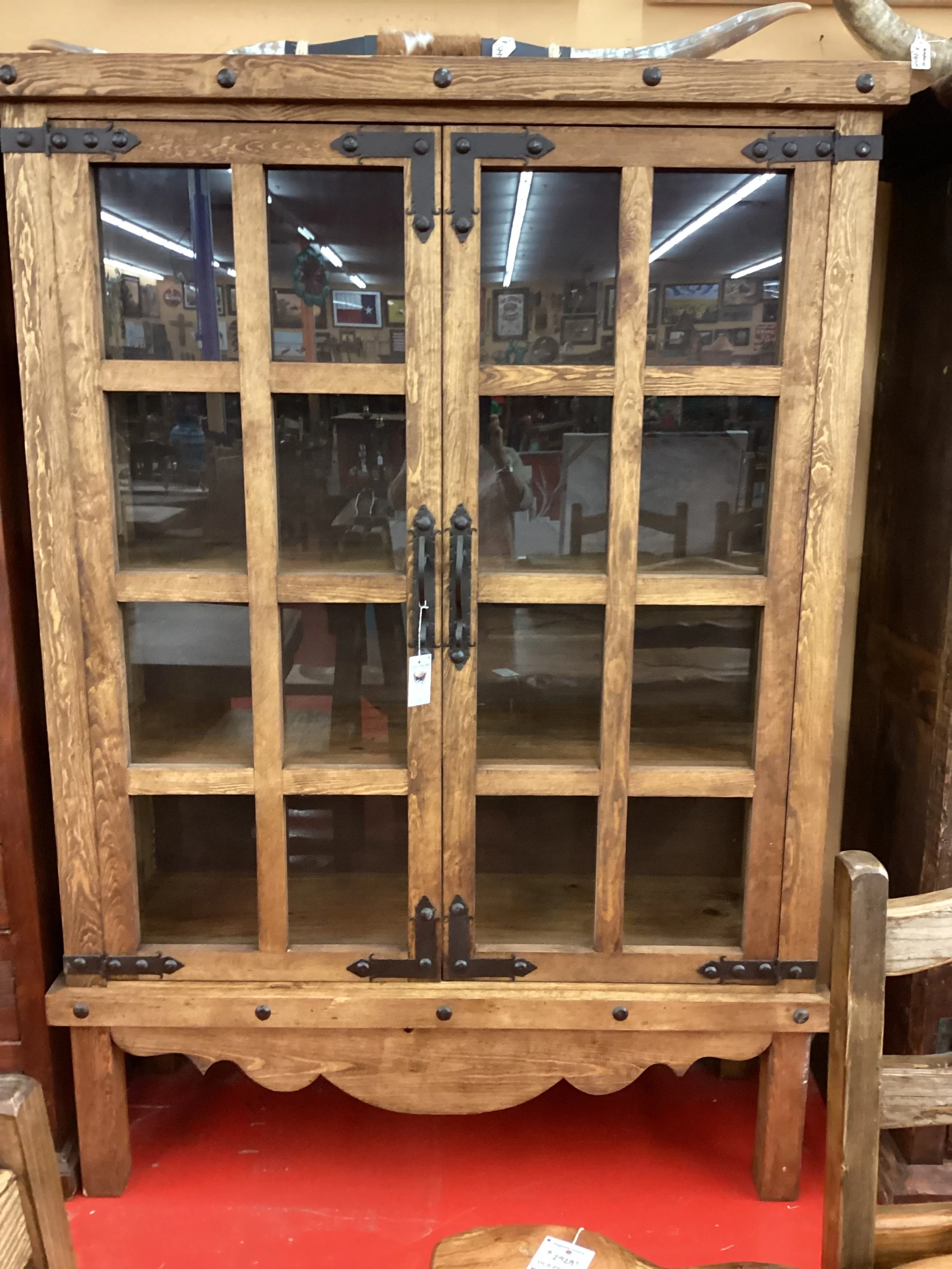 A wooden display cabinet with glass-paneled doors and black metal hardware, sitting on a red floor in a store.