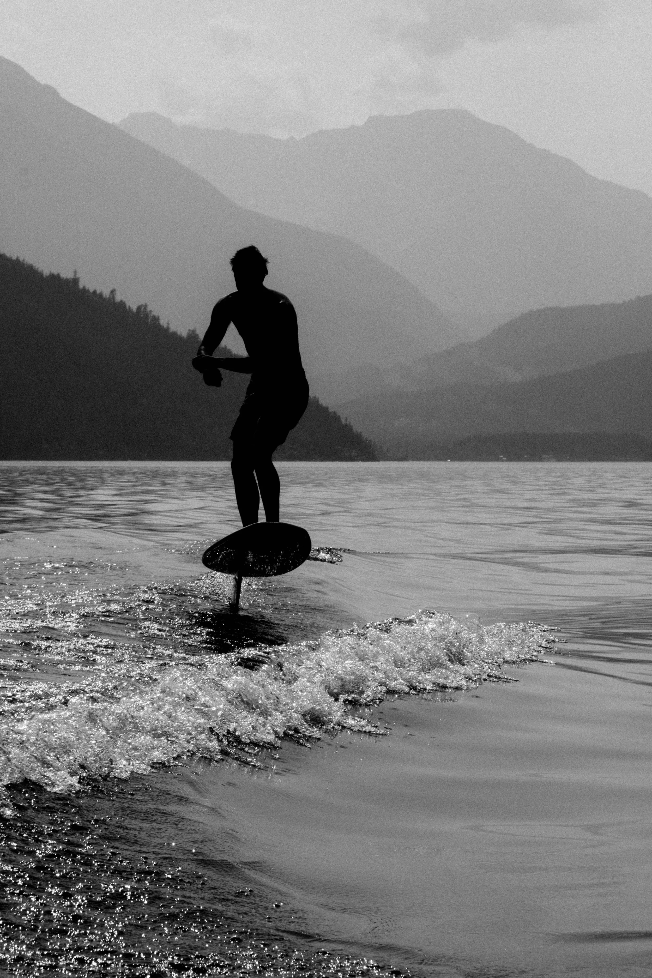 Silhouette of a person riding a paddleboard on a lake with mountains in the background in black and white.