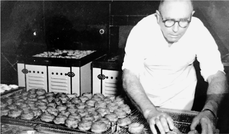 Black and white photo of a man in a bakery setting arranging baked goods on cooling racks.