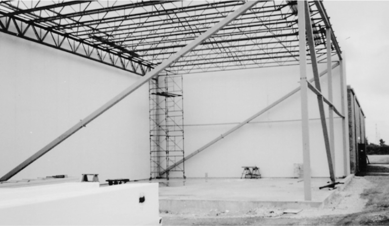 Black and white image of a building under construction, featuring a steel framework and scaffolding.