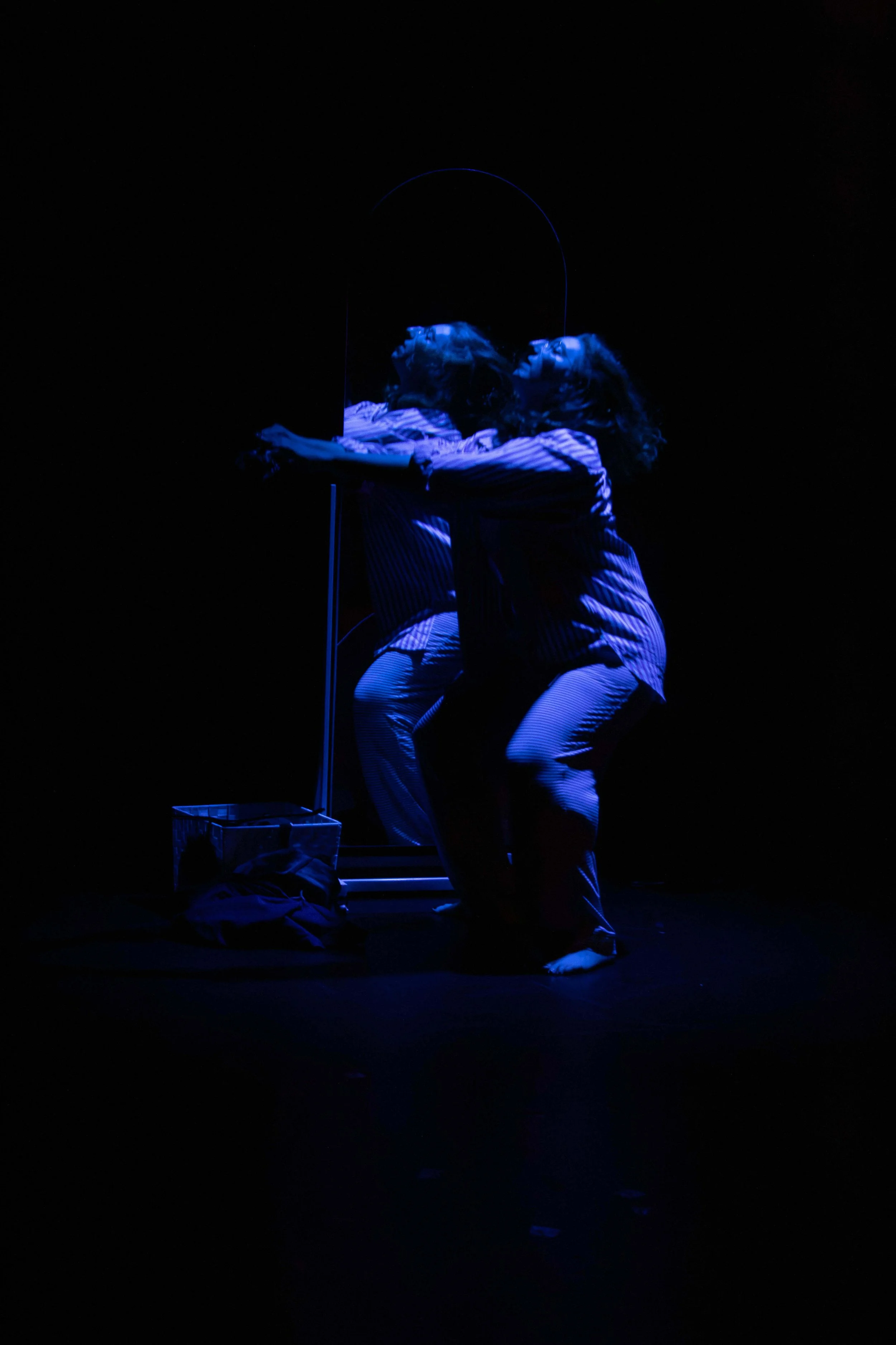 erformer Vanessa Meyer captured in dramatic blue stage lighting reaching toward a full-length mirror during a theatrical performance.