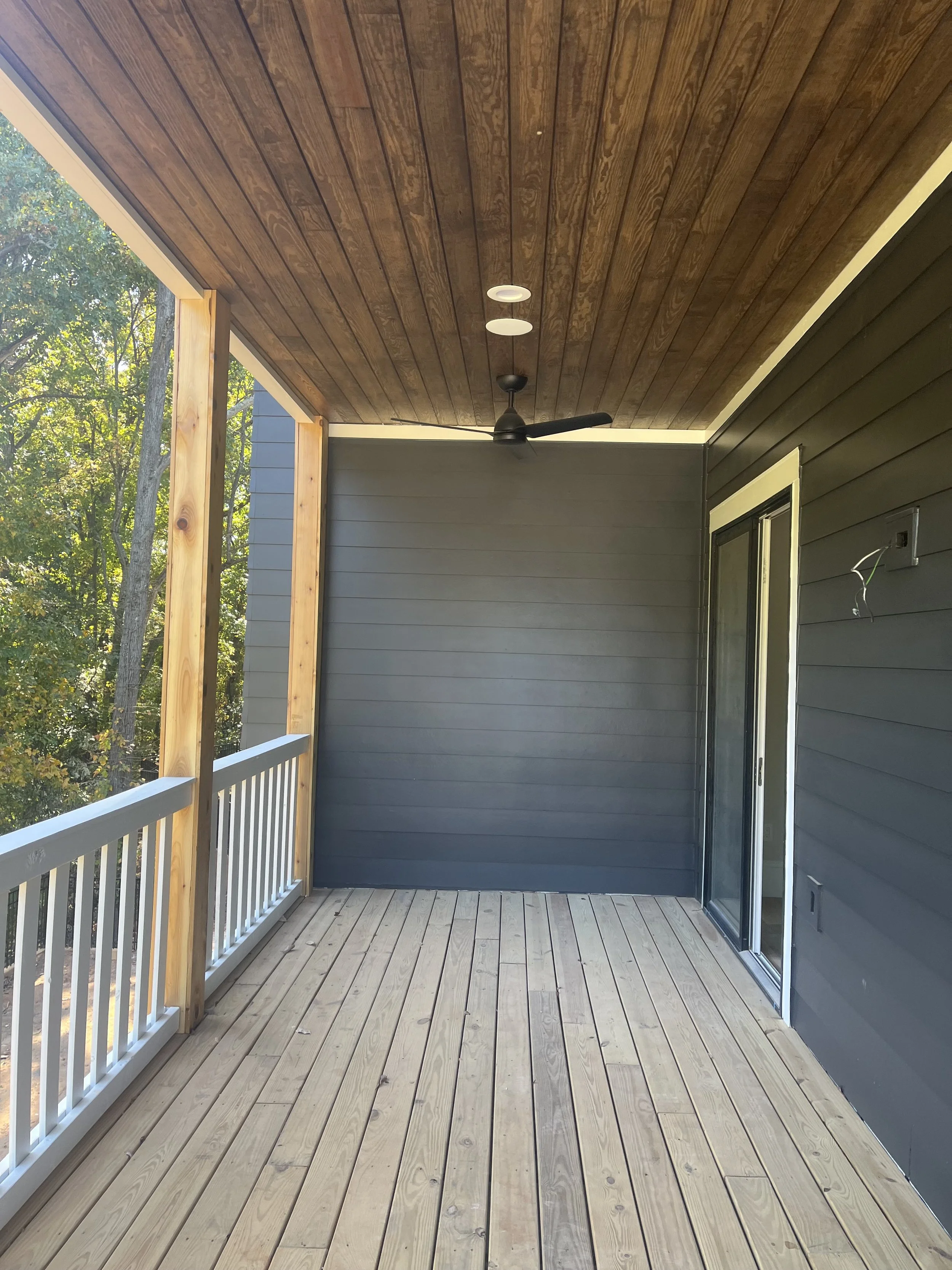 Exterior painting and wood finishing on a covered porch with dark siding.