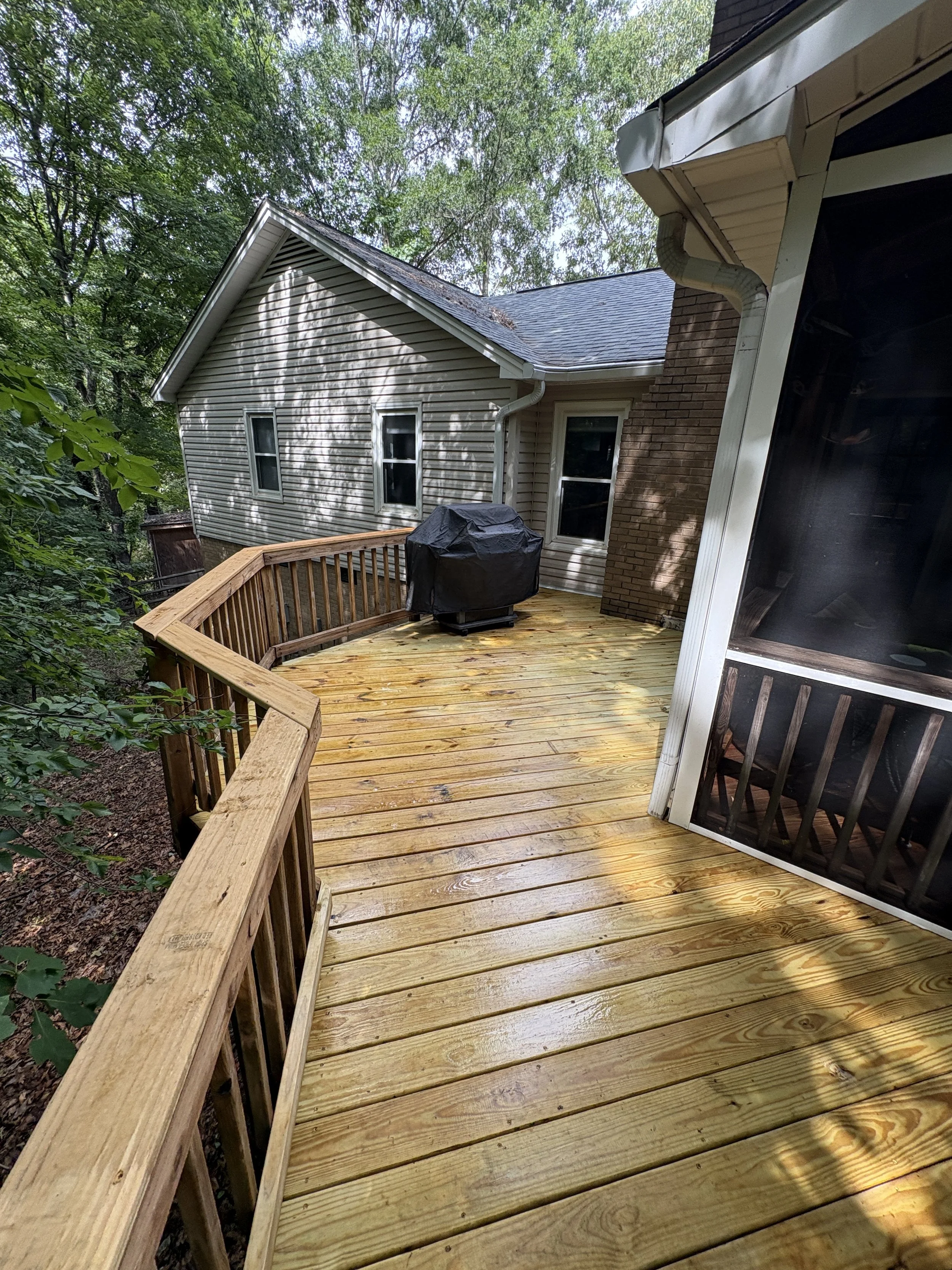 Wood deck and railing beside a screened porch, with a walkway leading toward the house.