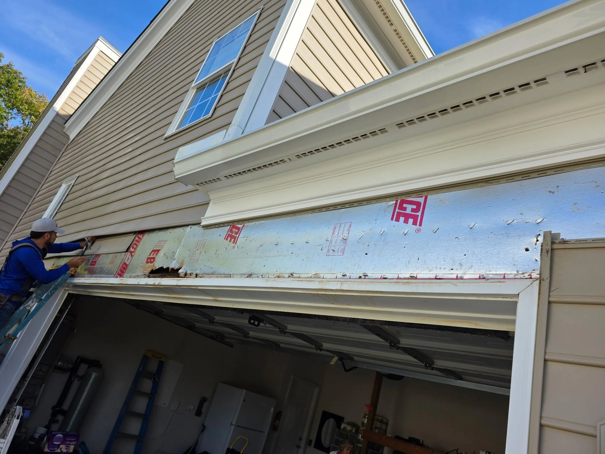 Garage-door header repair in progress with exterior trim removed and protective backing exposed, preparing the opening for flashing and trim reinstallation.