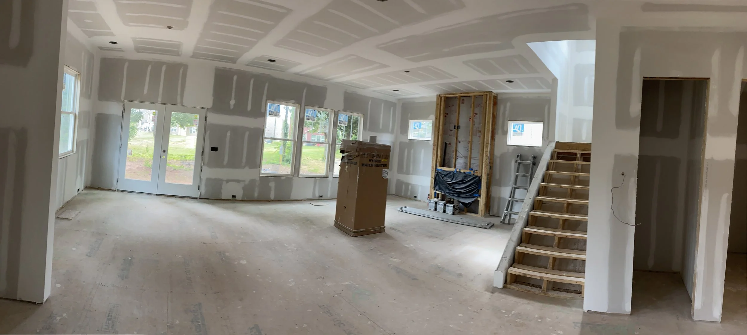 Wall and ceiling drywall installation in an open interior beside a staircase, with joint finishing in progress.