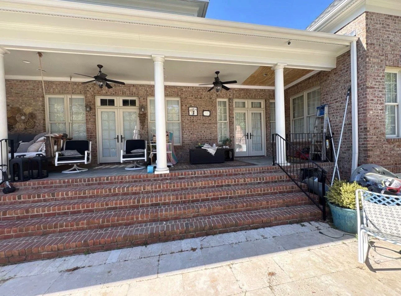 Wide view of a covered porch with white columns, ceiling fans, and brick steps.