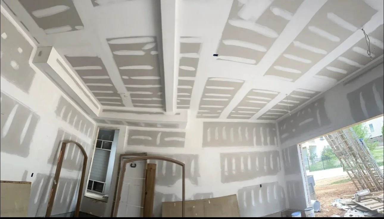 Drywall finishing across a room’s walls and ceiling, with joint compound covering panel seams and fasteners.