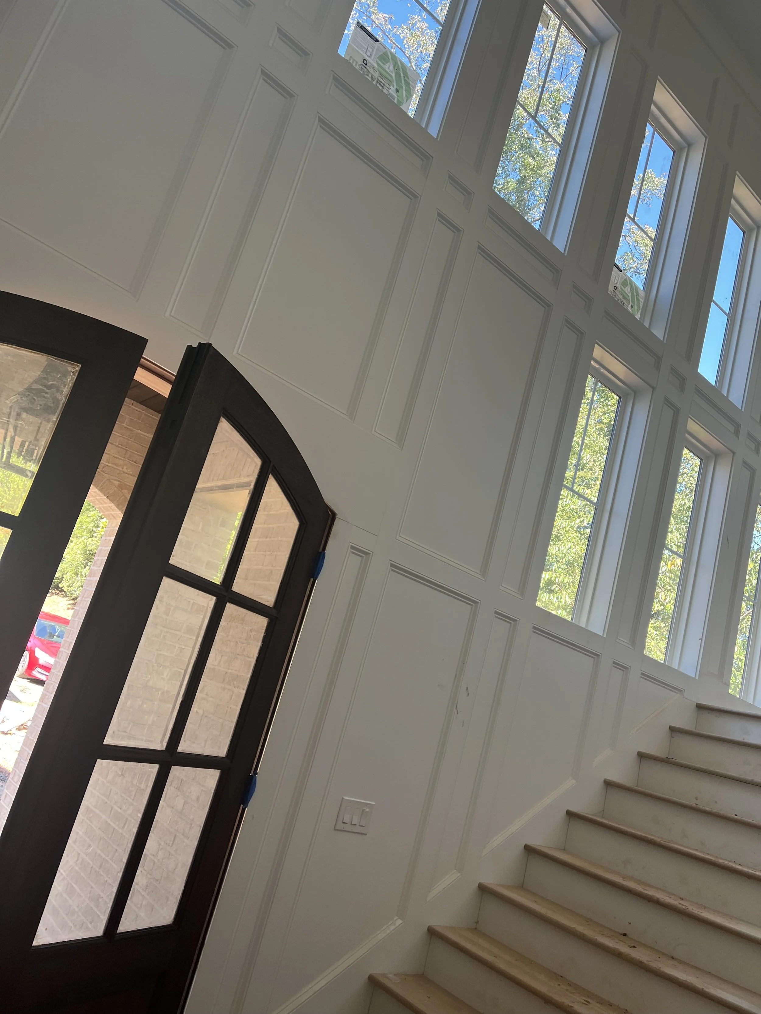 Interior foyer painting with tall windows, entry doors, and white wall trim.
