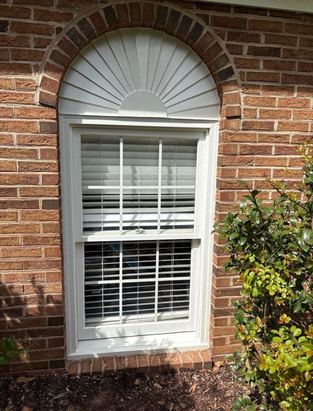 Exterior window with an arched top and white trim in a brick wall.