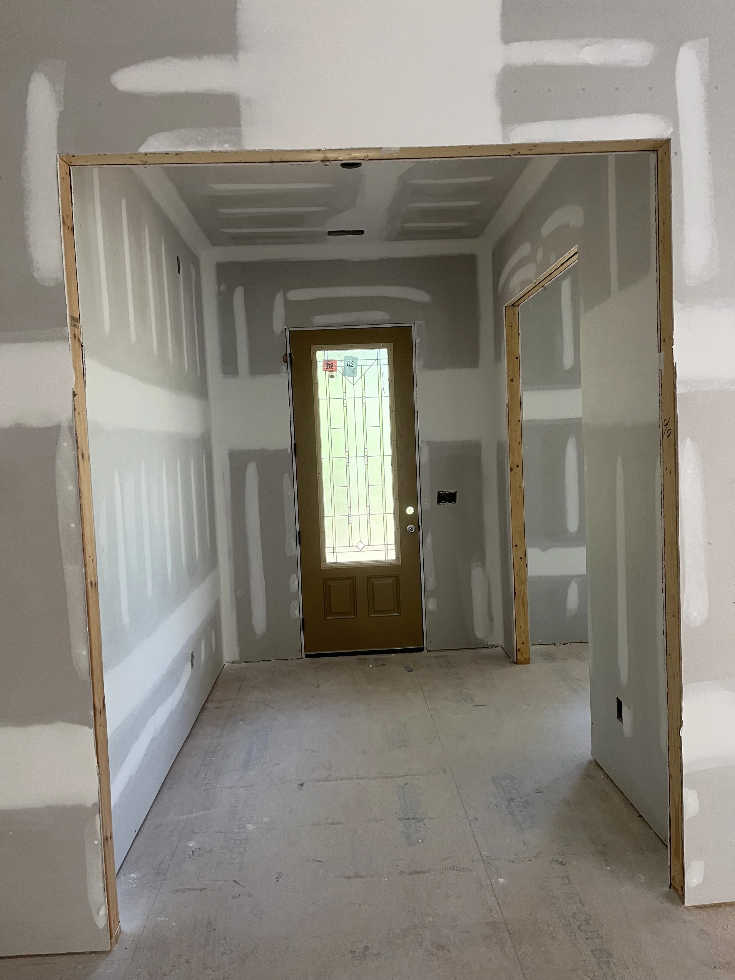 Wall and ceiling drywall installation in an entryway, with taped joints and joint compound around the exterior door.