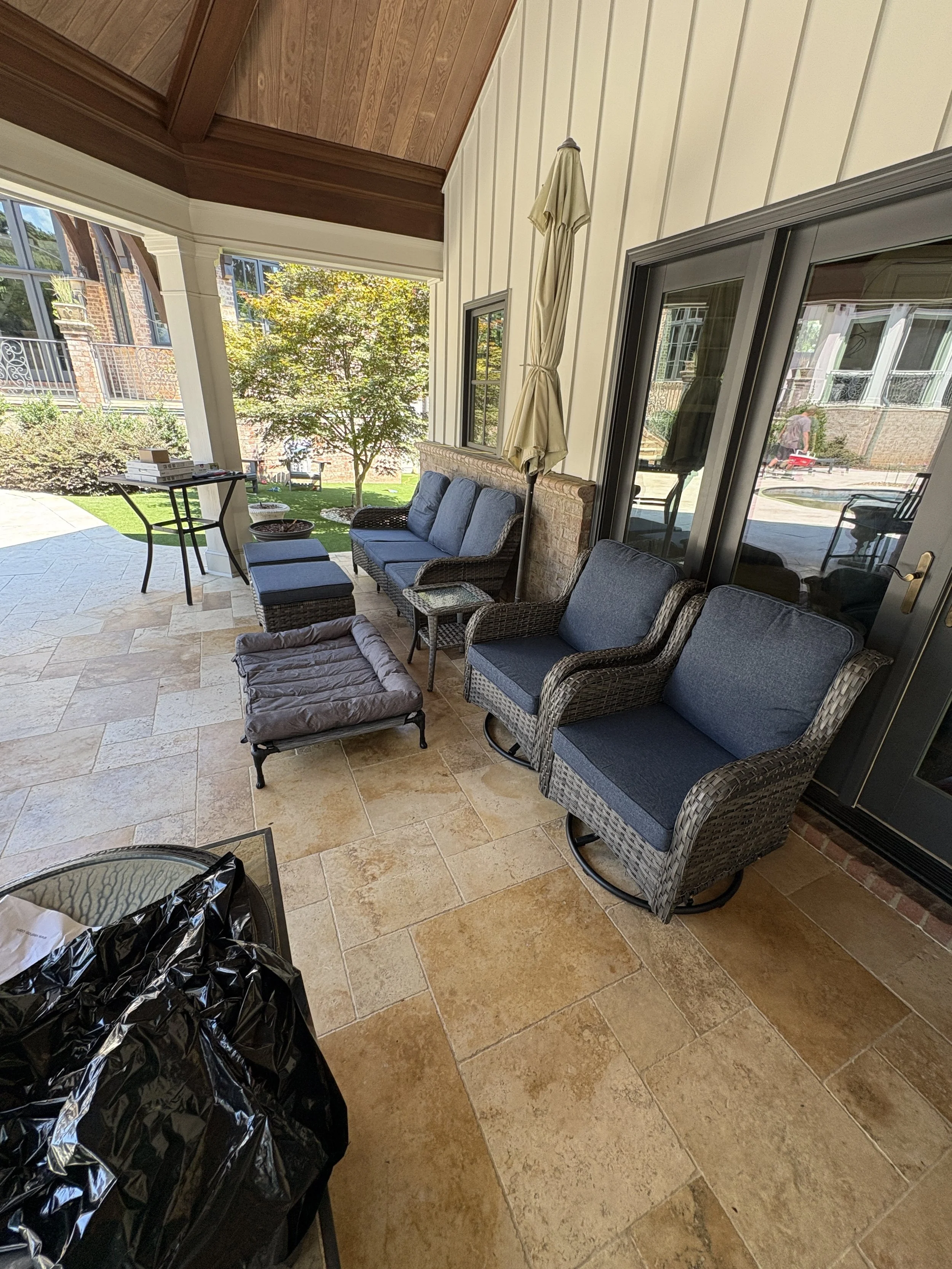 Covered patio with stone-look flooring and seating beside the home.
