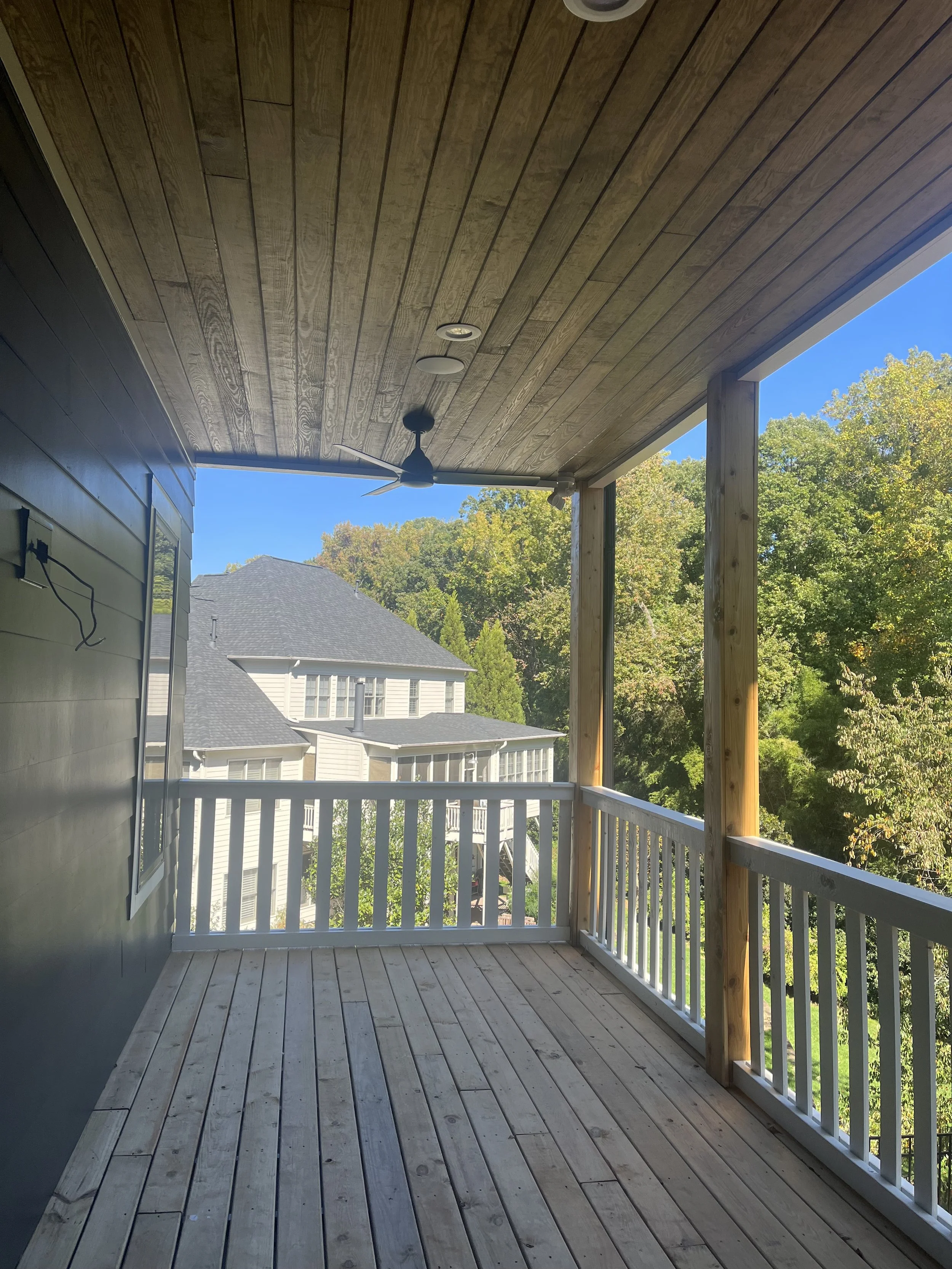 Covered porch with stained wood ceiling and painted railings.