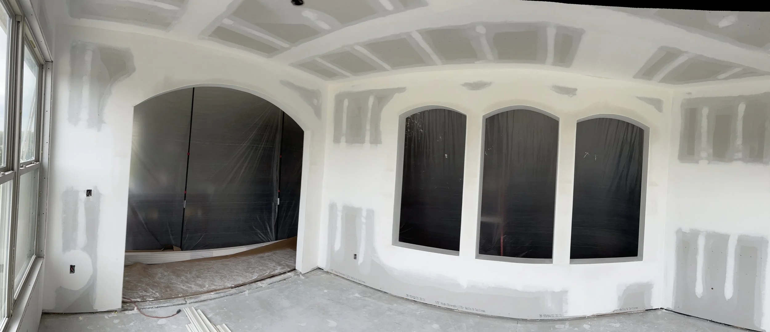 Drywall installed around arched wall openings, with taped joints across the walls and ceiling.