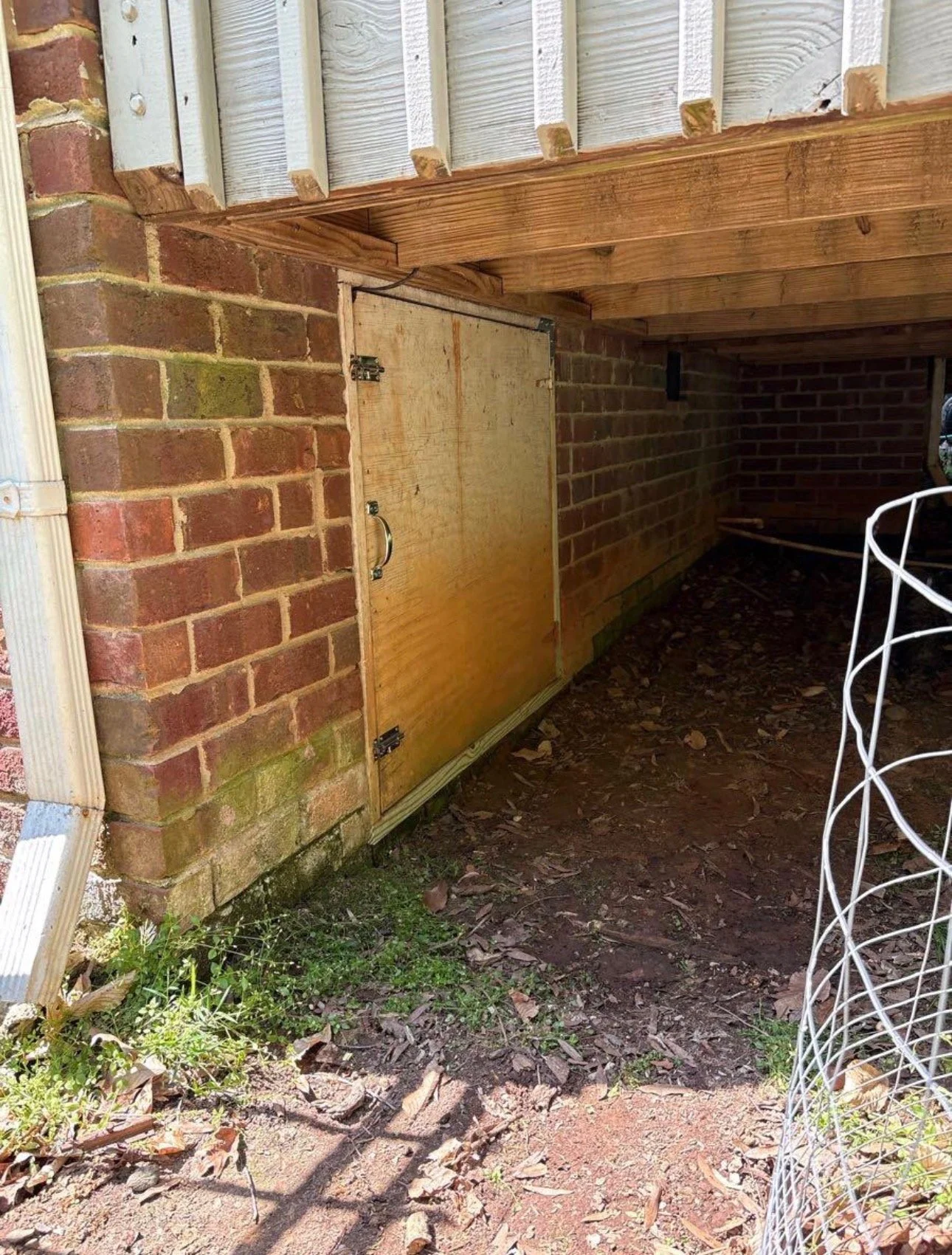 Wood access panel beneath a raised deck beside a brick foundation.