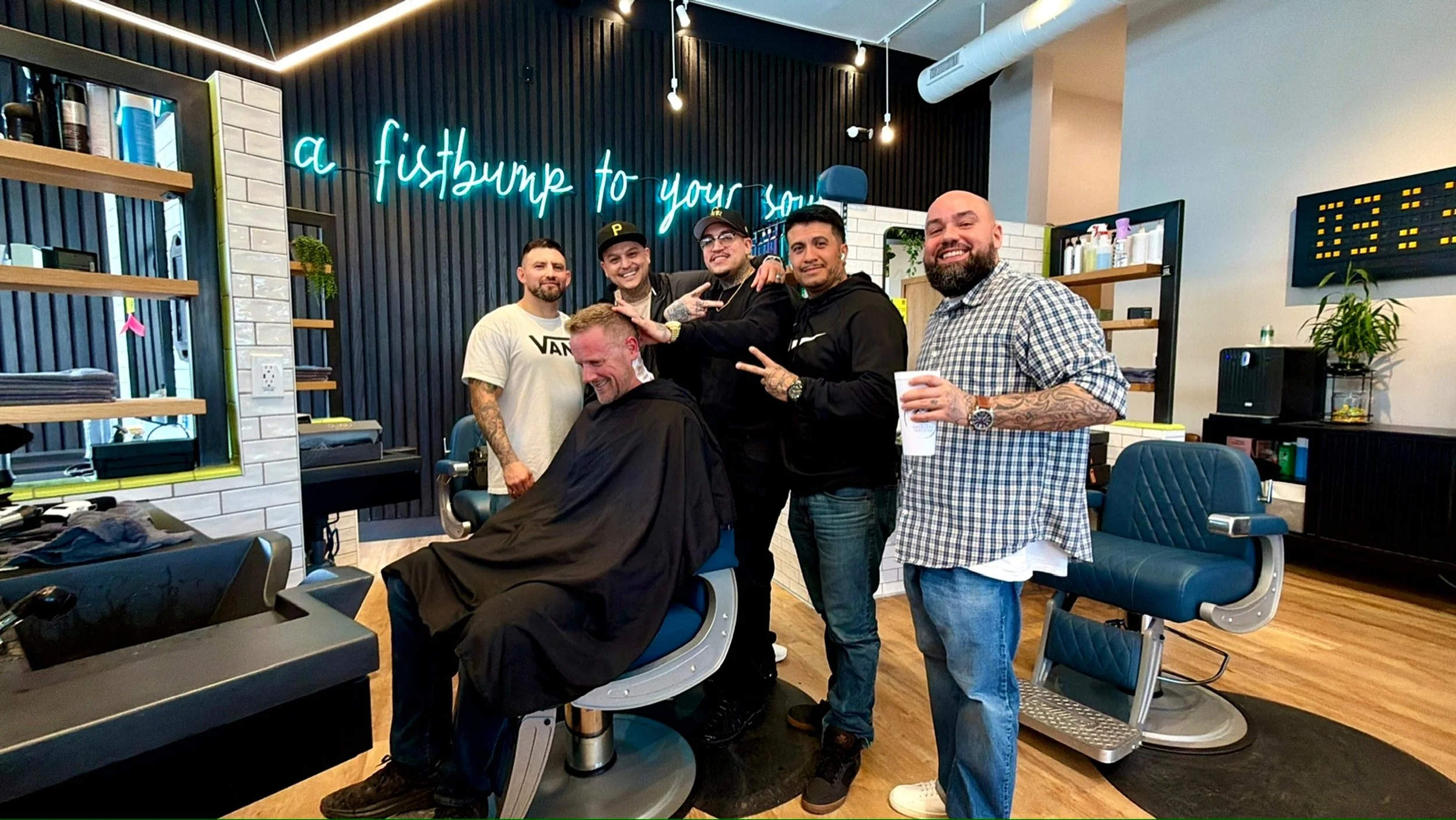James Repenning, CEO & Founder of R&R Head Labs, sits in barber seat surrounded by barber shop employees