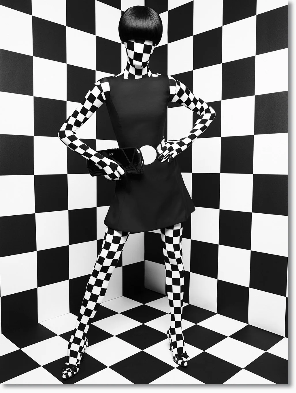 Schwarz-weiß-Foto einer Modepuppe mit schwarz-weiß-karierter Haut, in einer Karomuster-Wand- und Bodenumgebung, trägt eine schwarze Kleidung, Handschuhe und Schuhe mit Karomustern, hält eine schwarze Clutch, hat einen Bob-Haarschnitt.